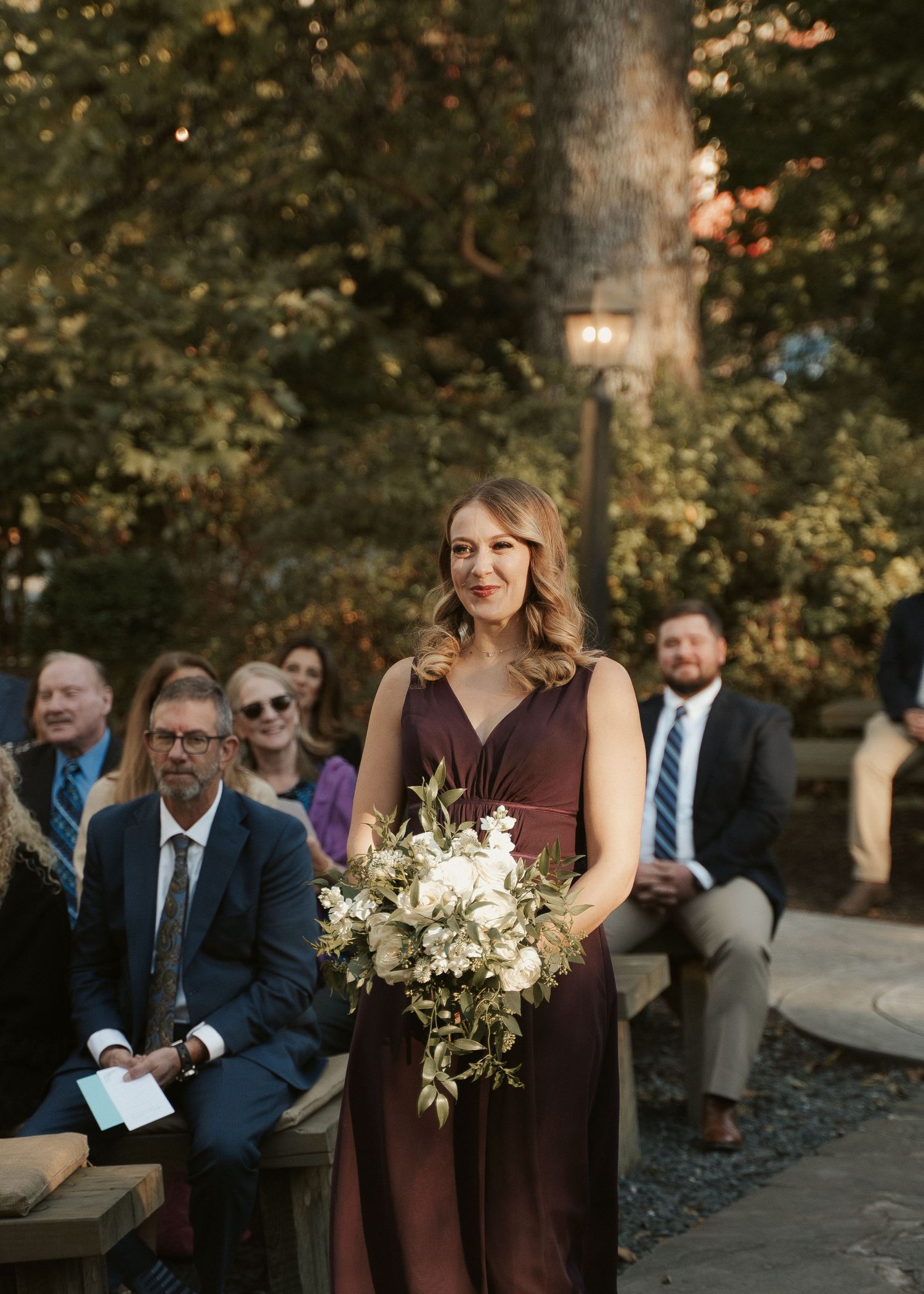 Bridesmaid walks down the aisle holding white bouquet during wedding ceremony at Mill at Fine Creek outside Richmond Virginia