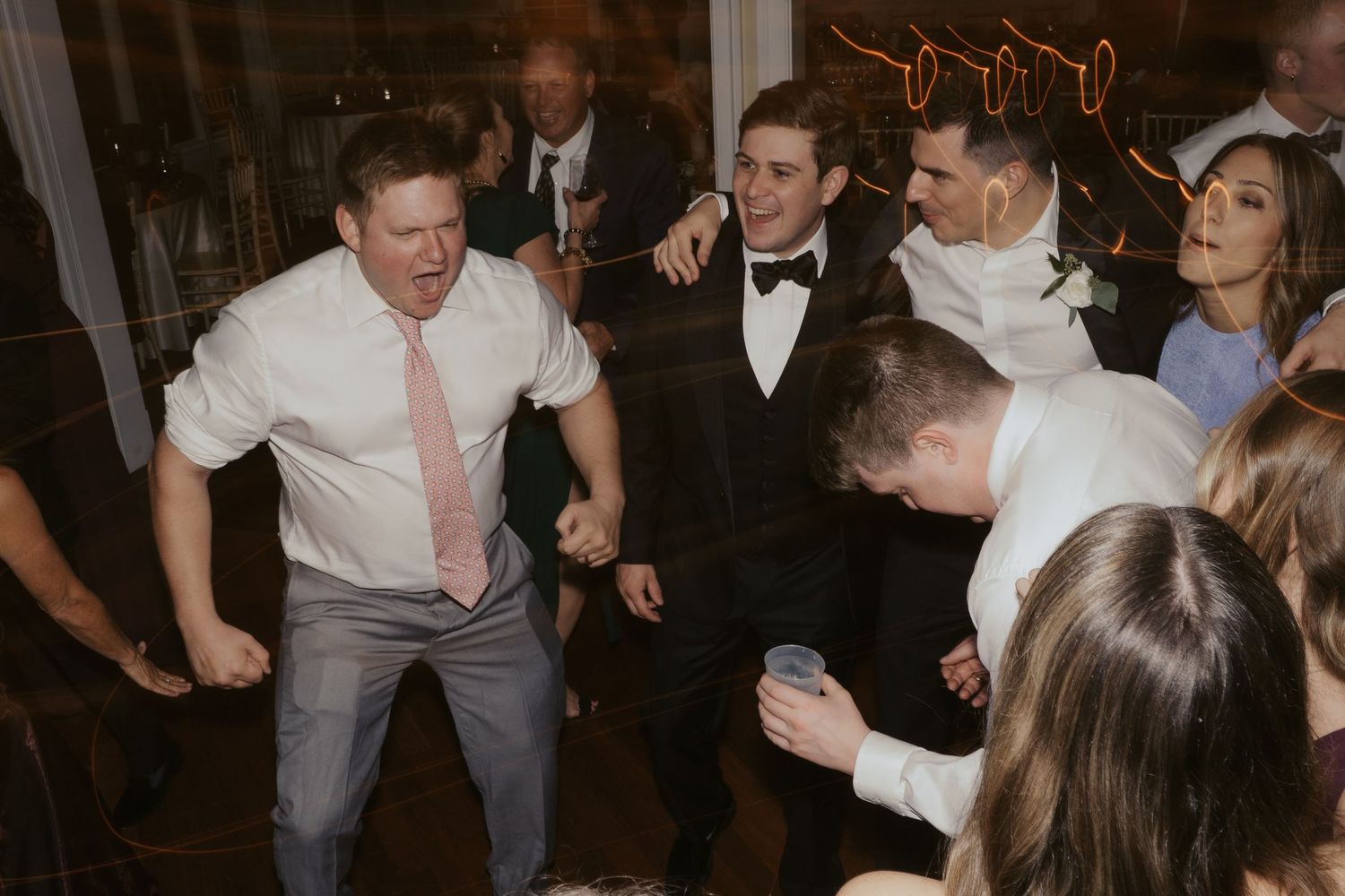 Groomsmen laugh as one of the groom's family members cheers on the dancefloor of a wedding reception at The Mill at Fine Creek
