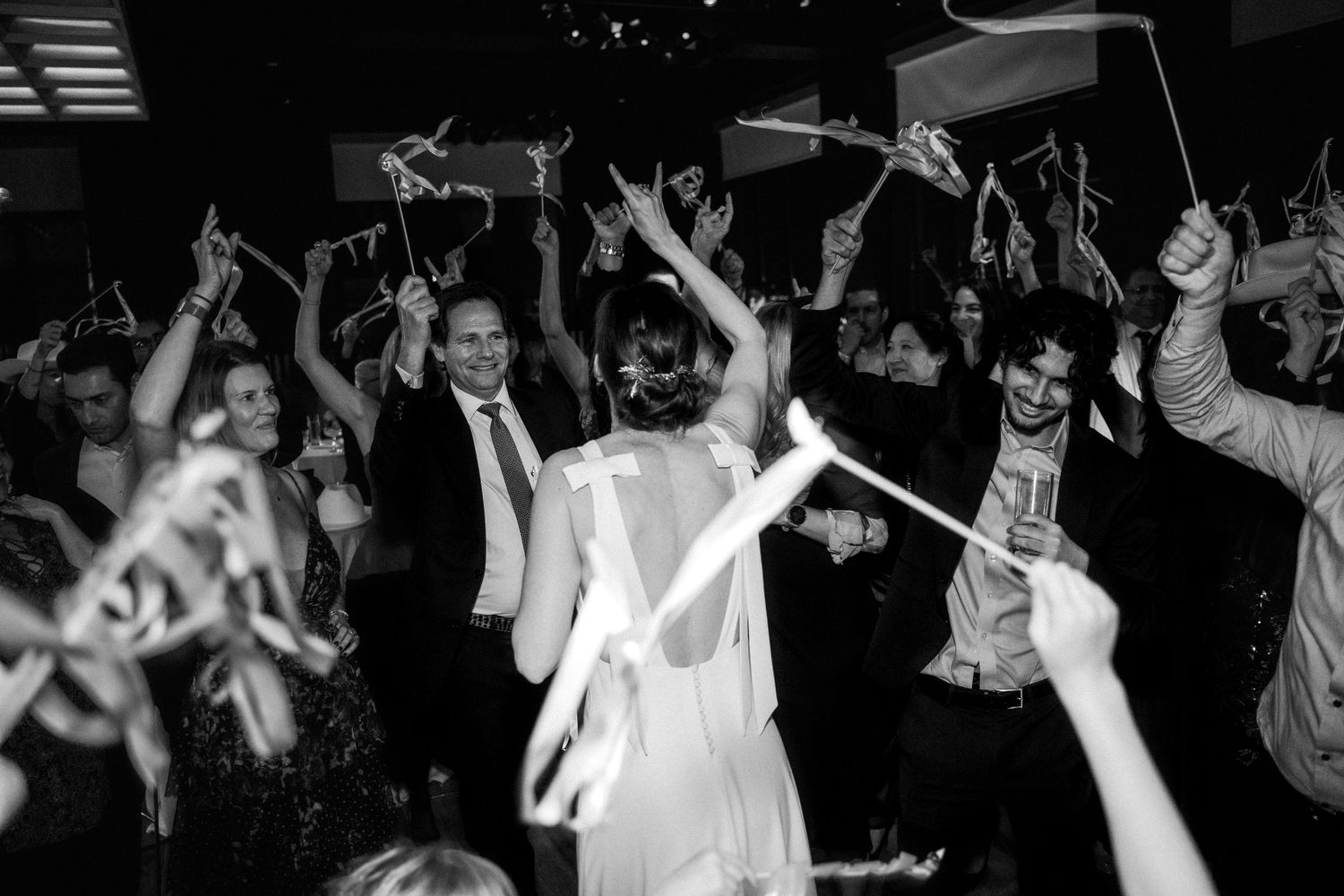 A Washington DC bride in a low-backed dress salutes the dancefloor full of guests with hookem horns at her Hotel Washington reception