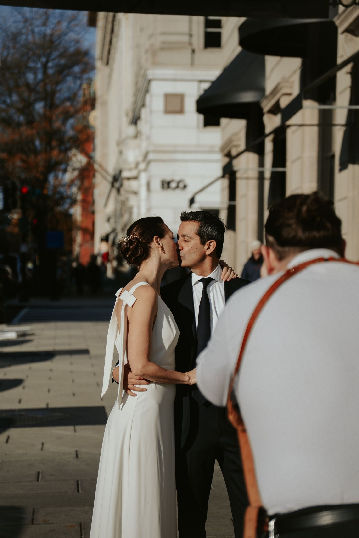 A Washington DC bride and groom kiss while their photo is taken underneath an awning by a photographer in the foreground