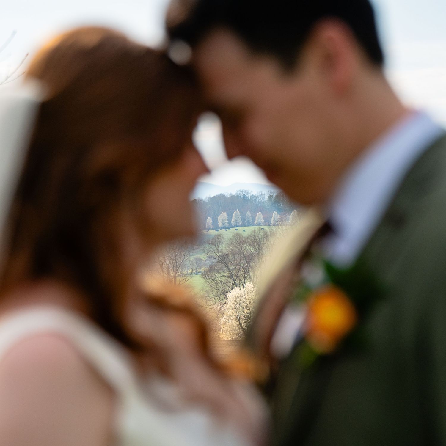 An out of focus bride and groom in the foreground stand touching foreheads while the Blue Ridge landscape is in focus in the background