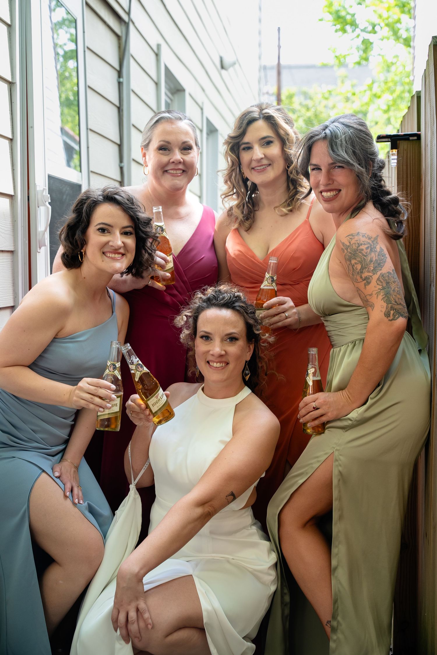 A bride crouches in front of her bridesmaids as they share Miller High Lifes prior to the Church Hill wedding ceremony in Richmond Virginia