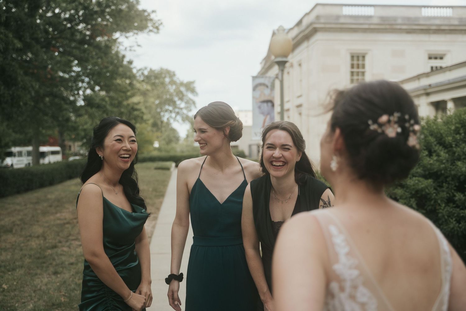 Three bridesmaids in green dresses smile at the bride before a ceremony at the Virginia Museum of Fine Arts in Richmond Virginia