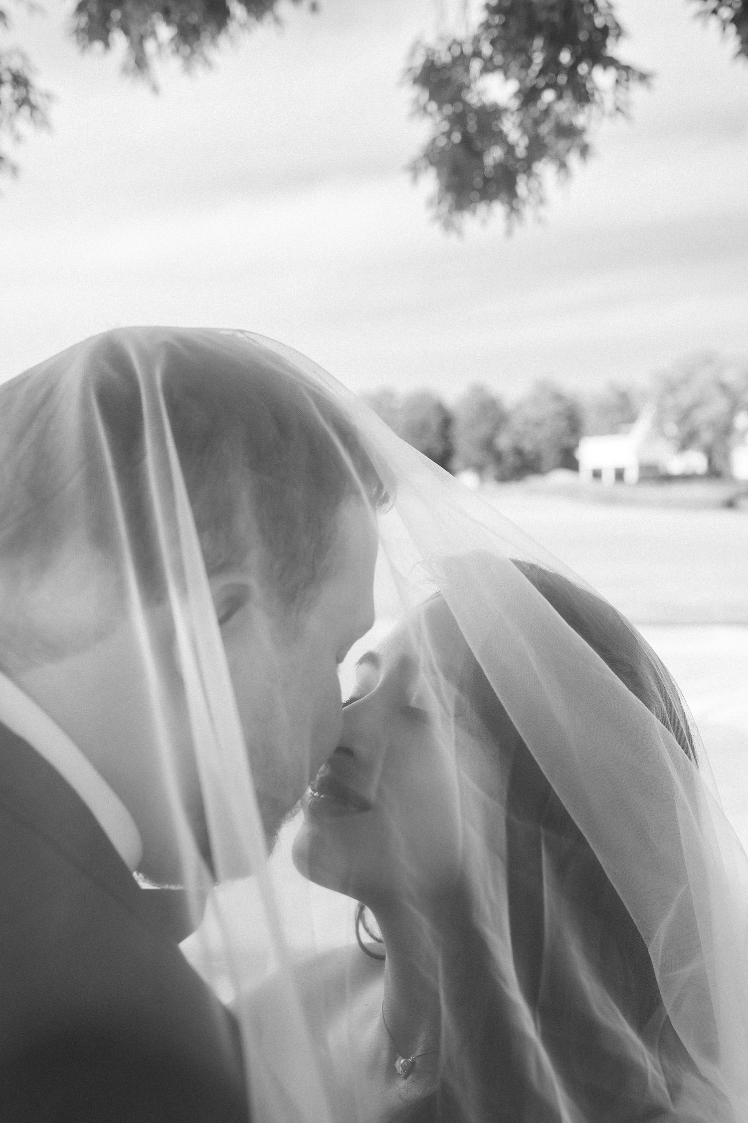 A bride and groom kiss under her veil in a dreamy black and white wedding portrait