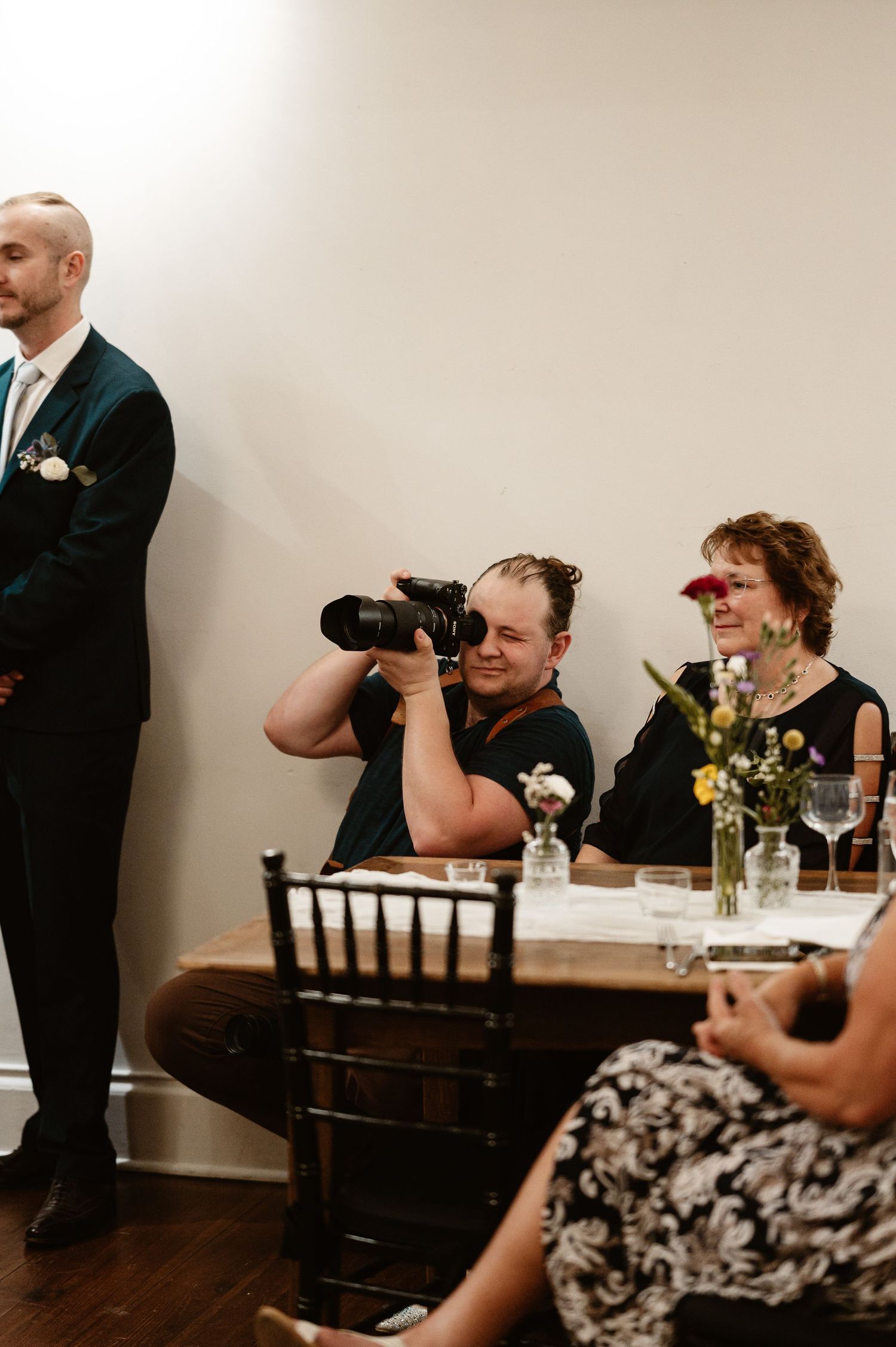 A wedding photographer crouches with a large camera up to his eye during a wedding in Charlottesville, Virginia
