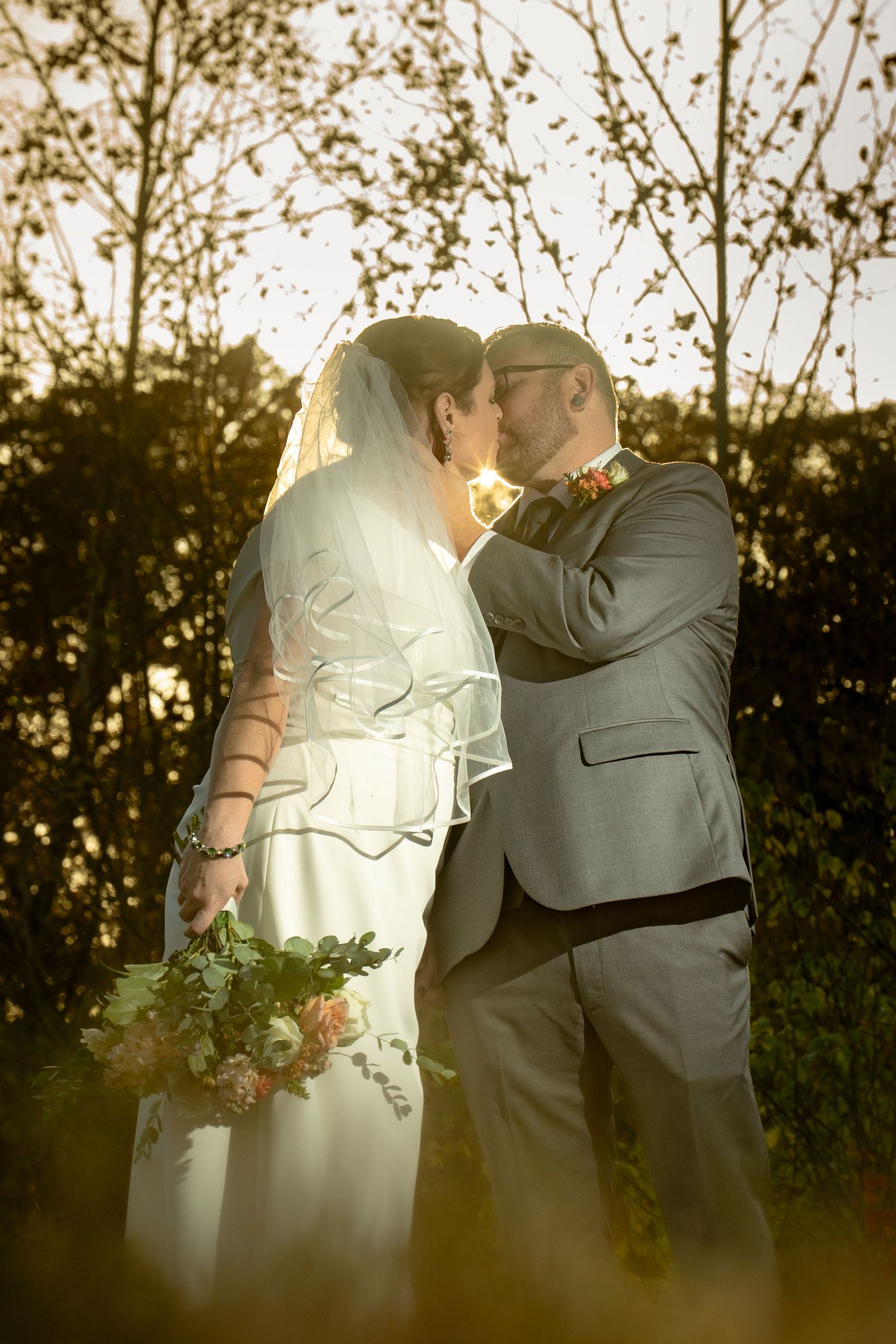 Virginia bride in a white dress kisses her husband in a gray suit during sunset newlywed portrait.