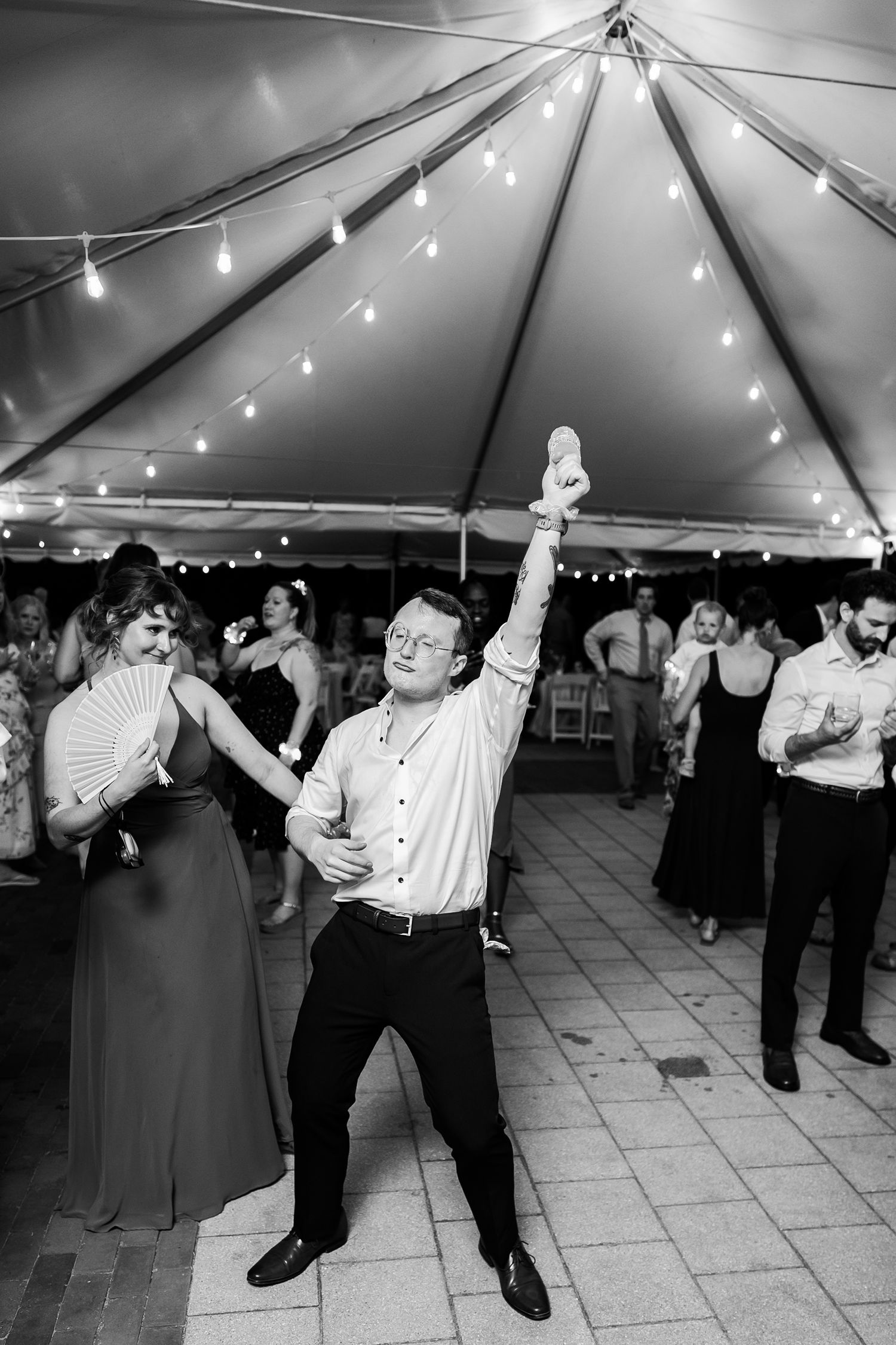 Virginia groomsman lifts his arm to the ceiling under the tent of the wedding venue at Lewis Ginter Botanical Gardens