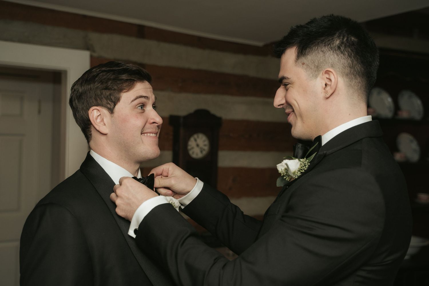 A groomsmen smiles while fixing the groom's tie as they prepare for the wedding ceremony at Mill at Fine Creek outside Richmond Virginia