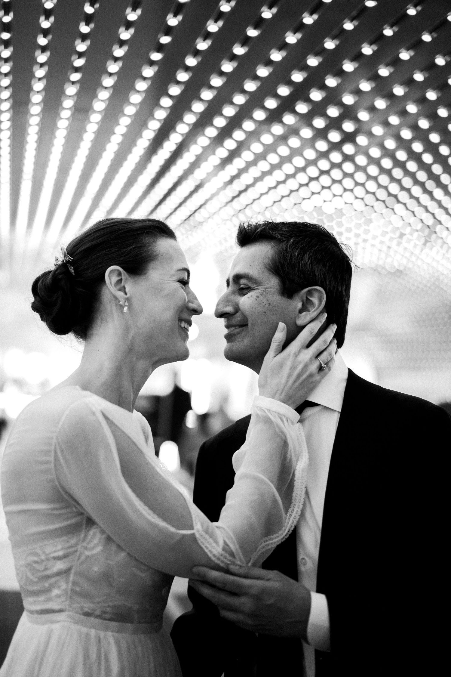 Bride in flowy wedding dress cups her husband's face under starry lights documentary style in the underground of the National Gallery of Art