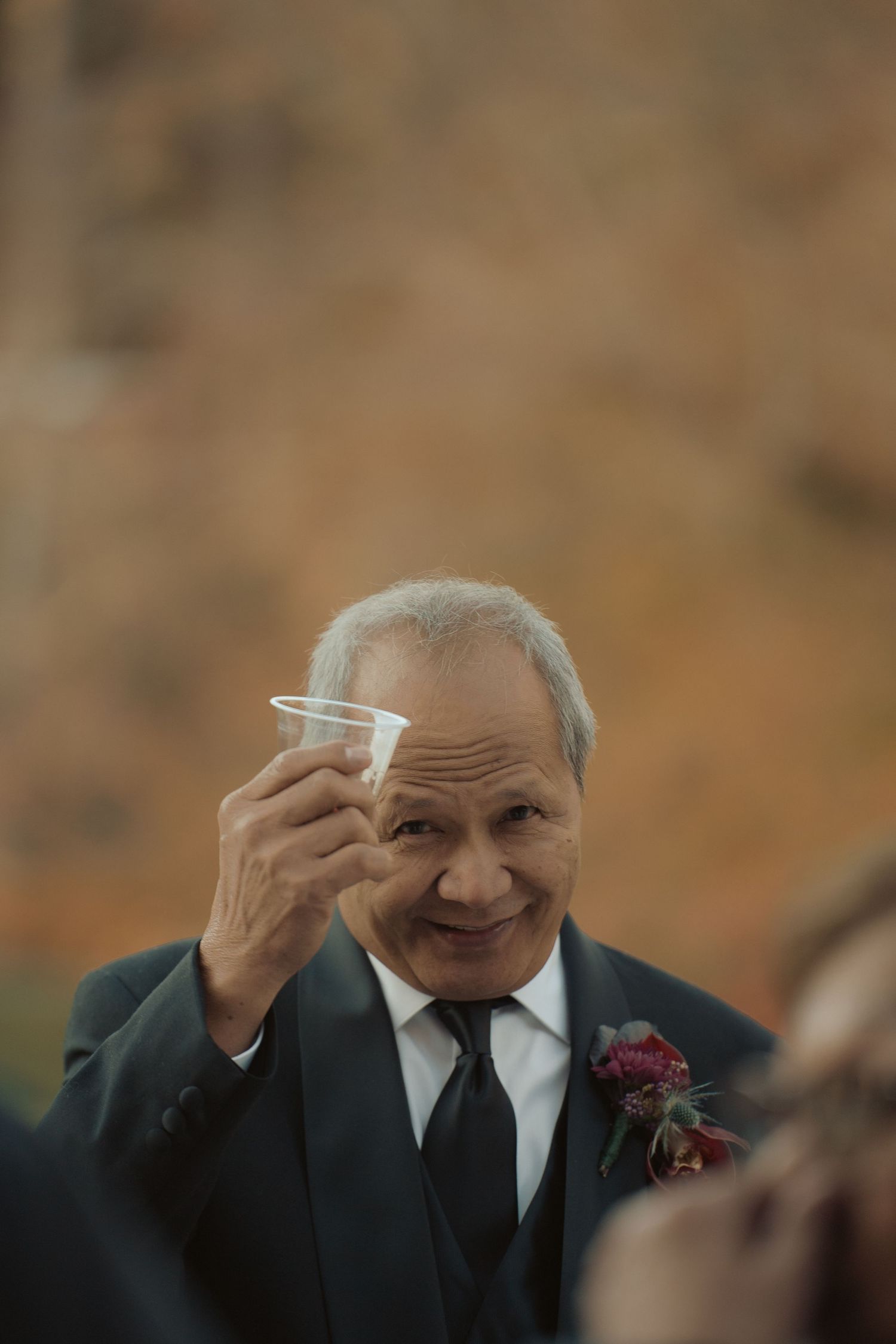 Portrait of queer bride's father holding up a drink at cocktail hour towards the camera of documentary wedding photographer in Maryland