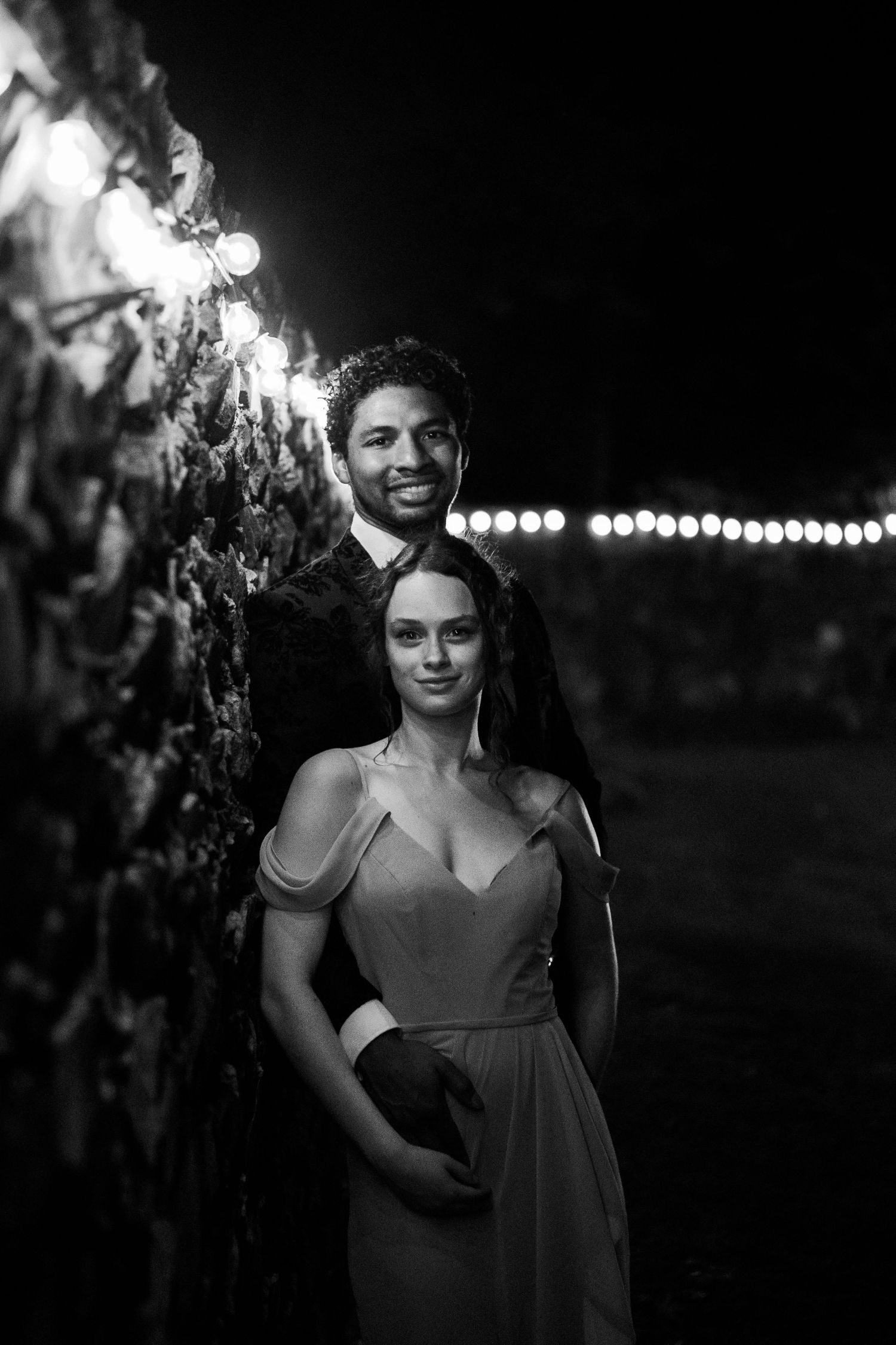 Wedding bridesmaid and her boyfriend pose for a nighttime portrait with fairy lights during a central Virginia wedding