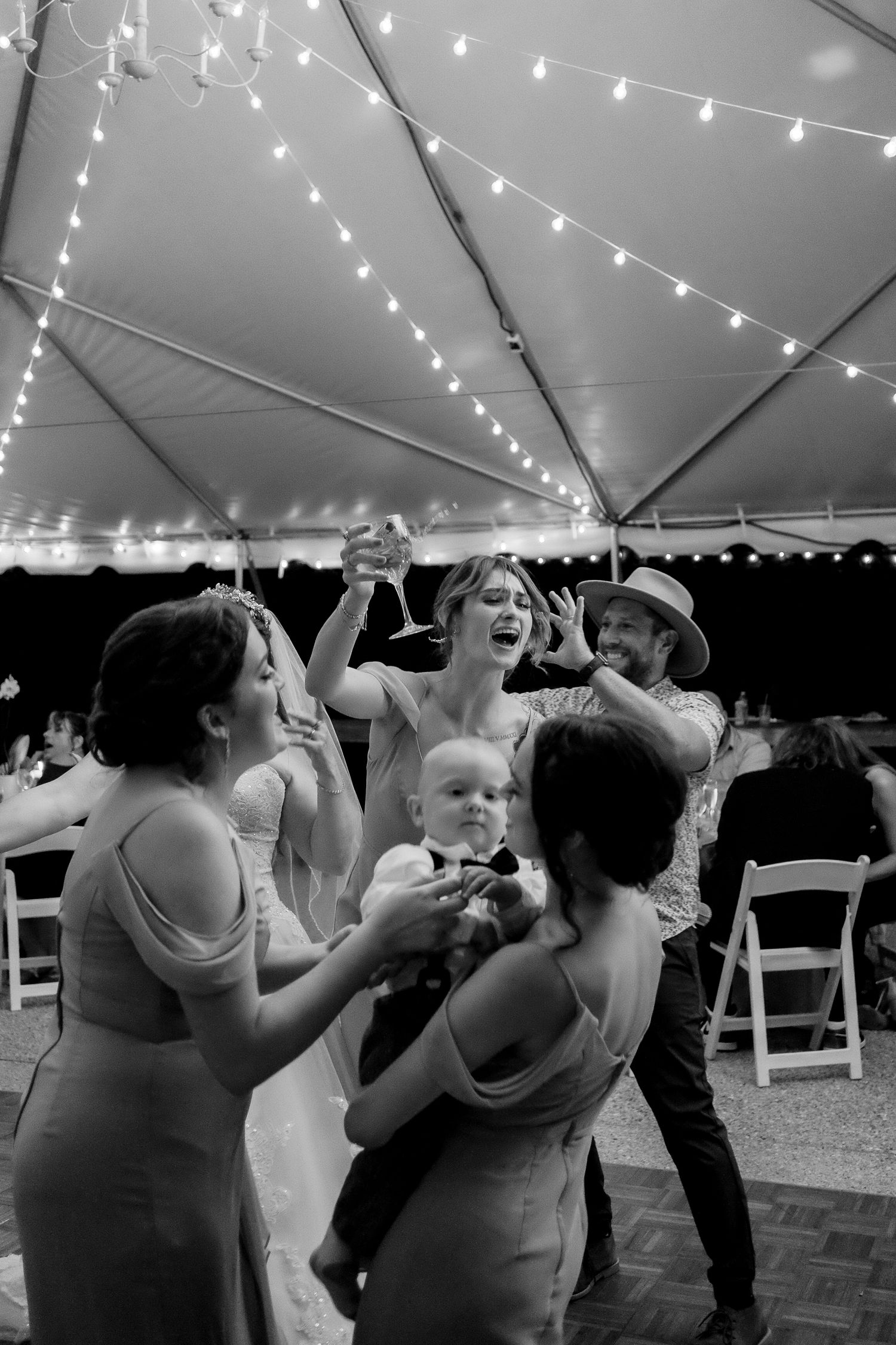 Wedding bridesmaid screams along to song while holding a wine glass while her baby is held in the foreground