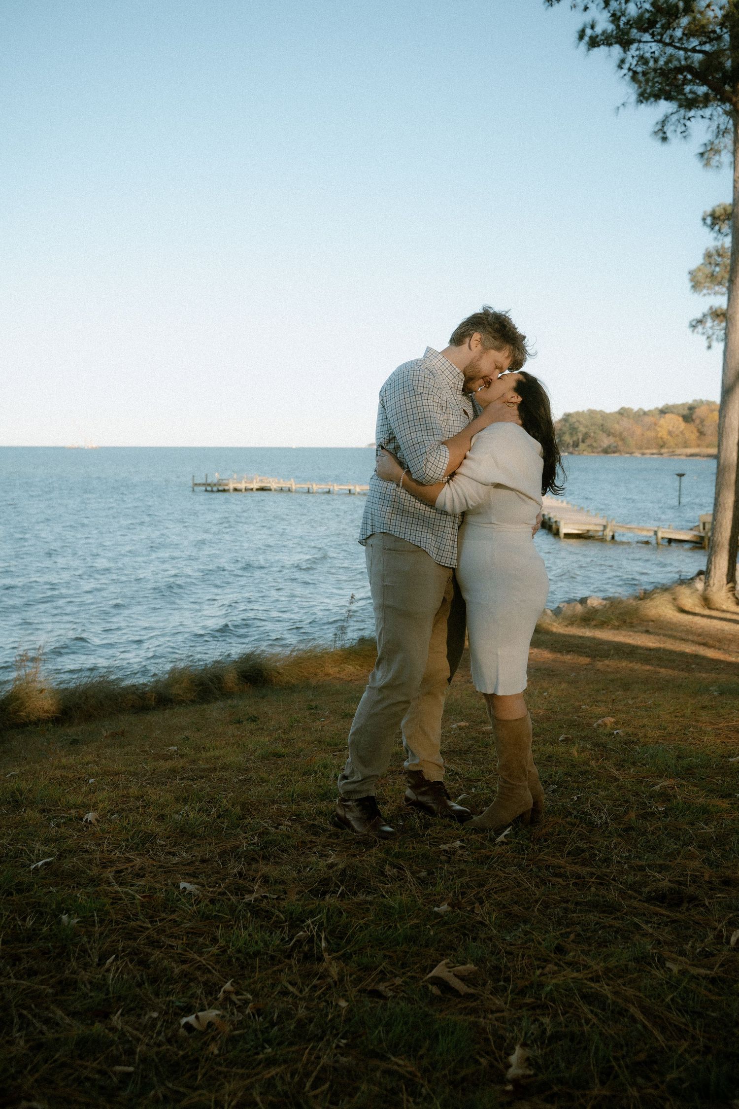 Modern, timeless engagement shoot in front of outdoor lake featuring light blues, couple kisses in foreground