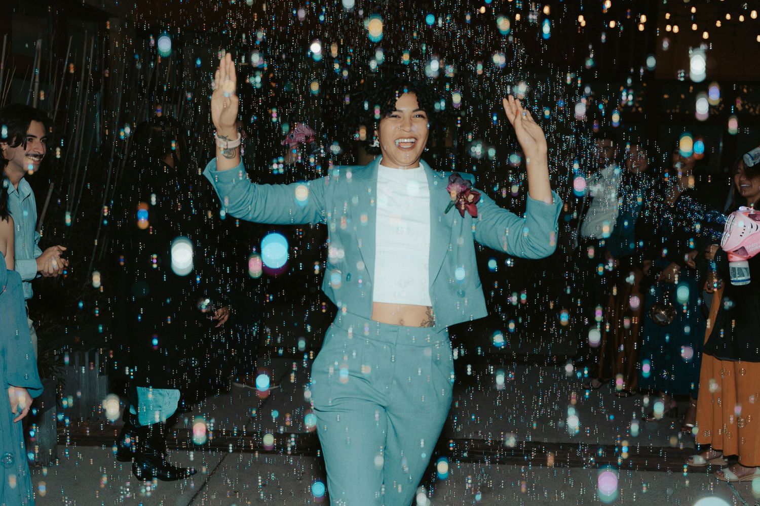 A queer wedding bridesmaid exits the reception through a cloud of bright bubbles at a venue in Maryland