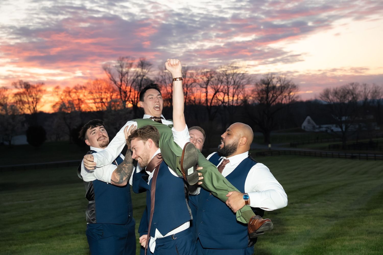 Groomsmen carry the groom in fun documentary style wedding party photo during sunset of a wedding in the Shenandoah Valley of Virginia
