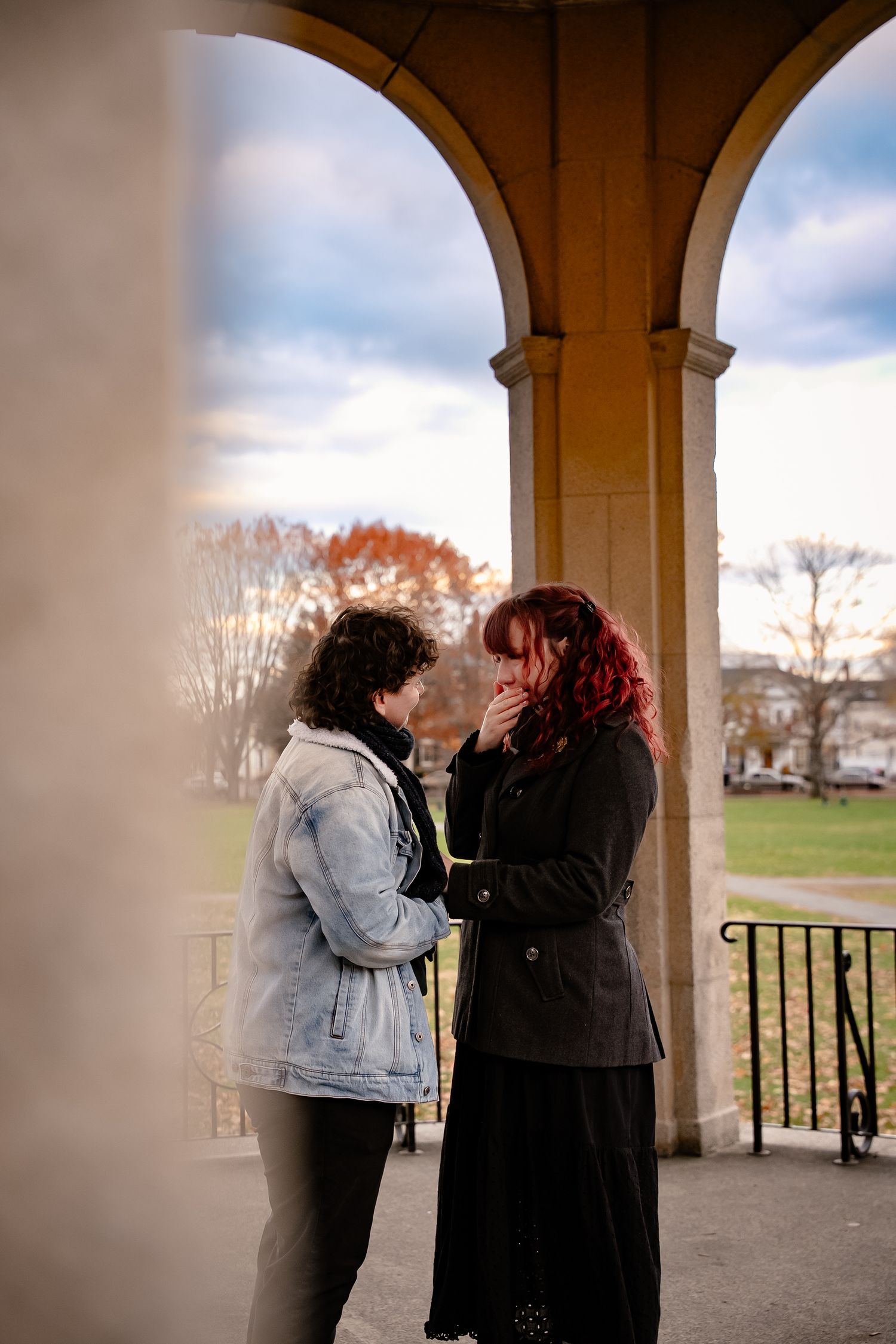 Lesbian couple smile with tears in their eyes at a historic witchy Salem, Massachusetts engagement and surprise photo session
