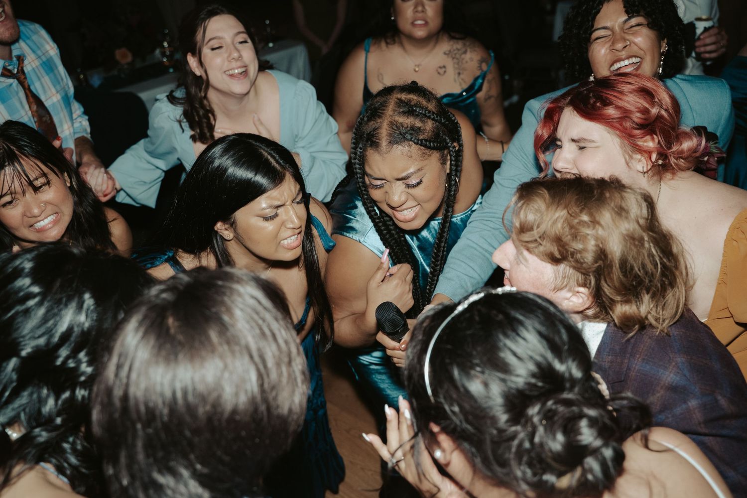 A group of friends & Bridesmaids lean in to sing karaoke together on the dancefloor of a queer wedding in Maryland