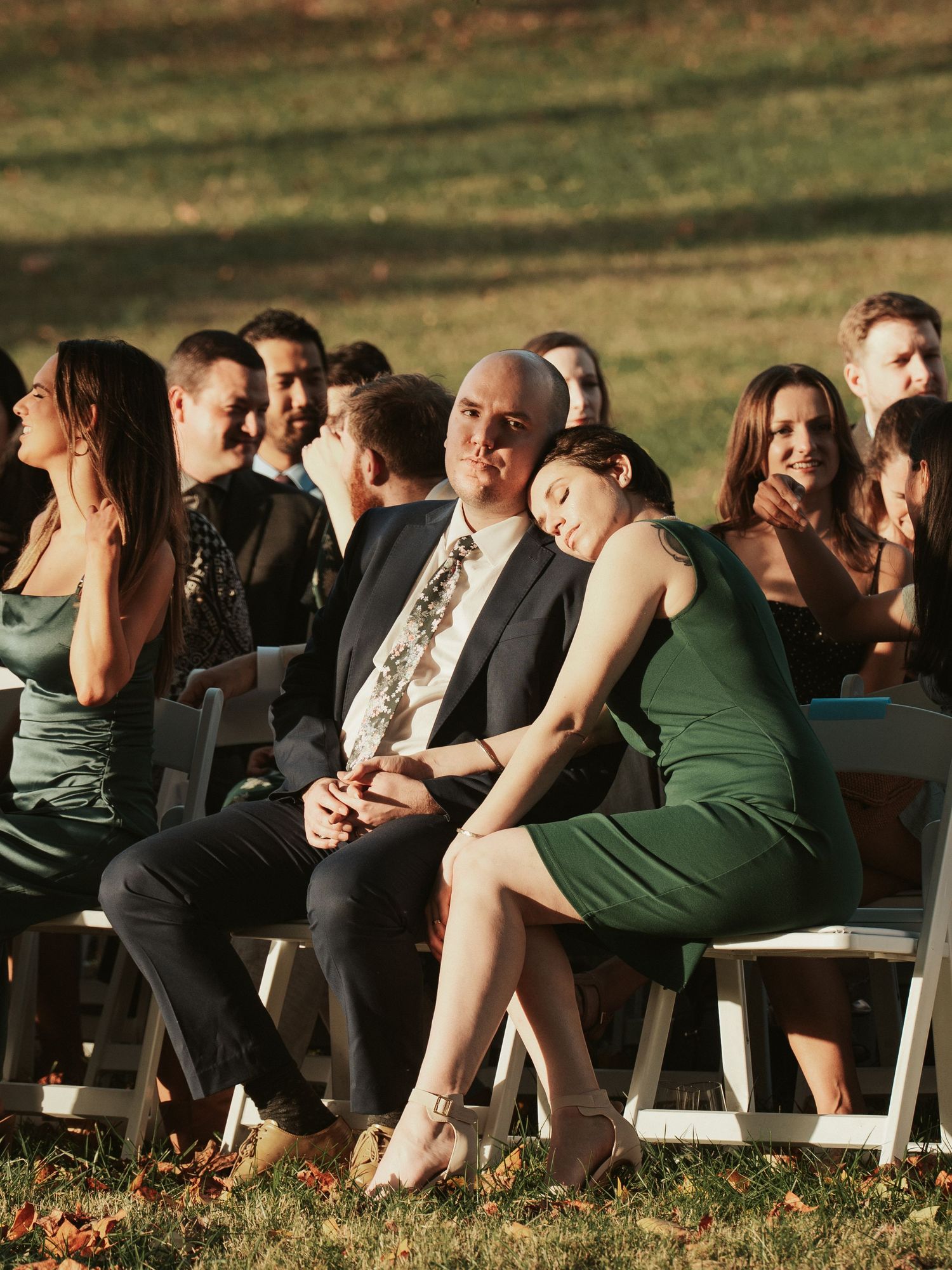 A wedding guest leans on her partner while he looks at the camera during a sweet gay wedding ceremony at Maymont Park in Richmond Virginia