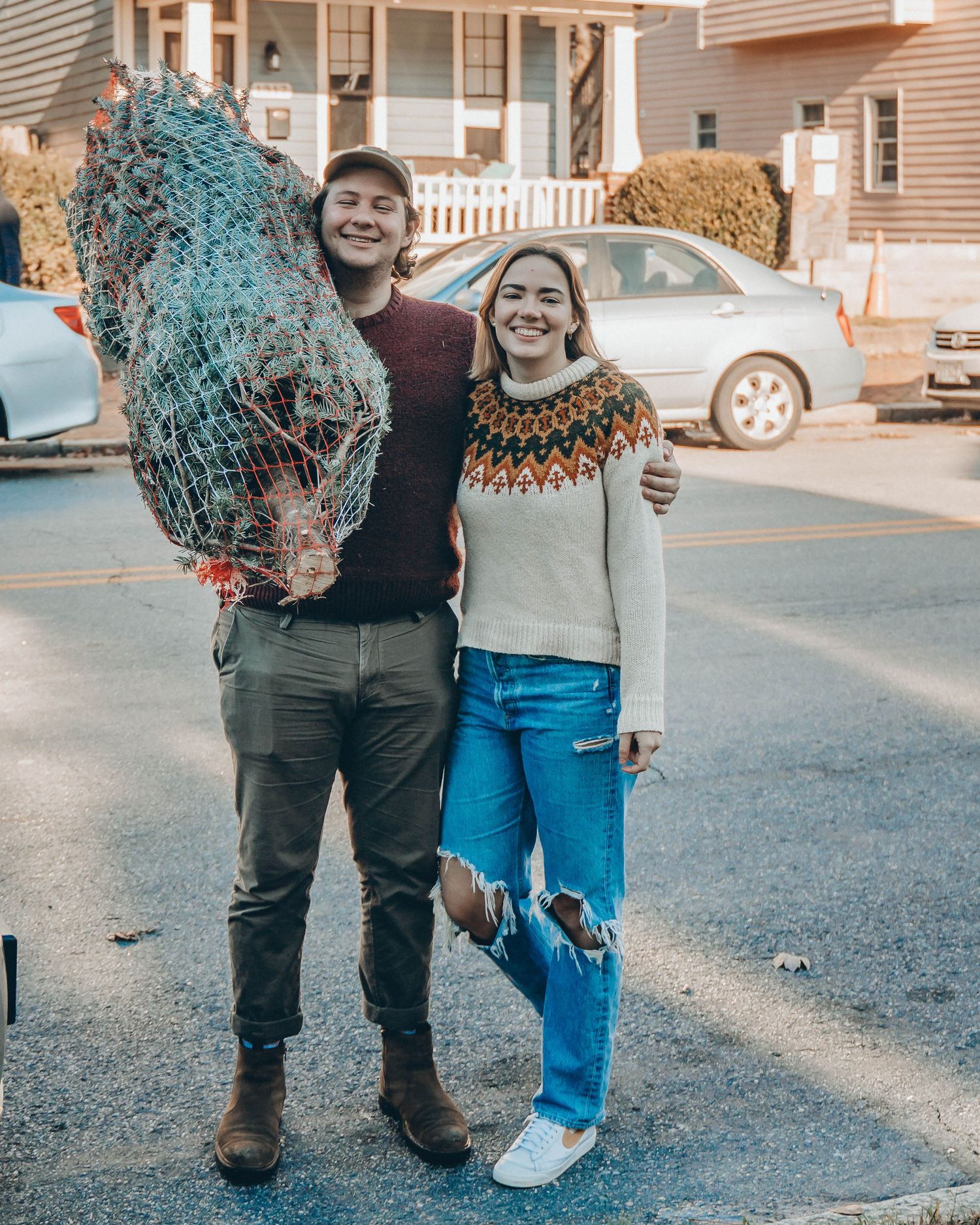 Queer wedding and event photographer based in Maine, Daniel Bowler, and his non-binary partner pose wearing sweaters with Christmas tree