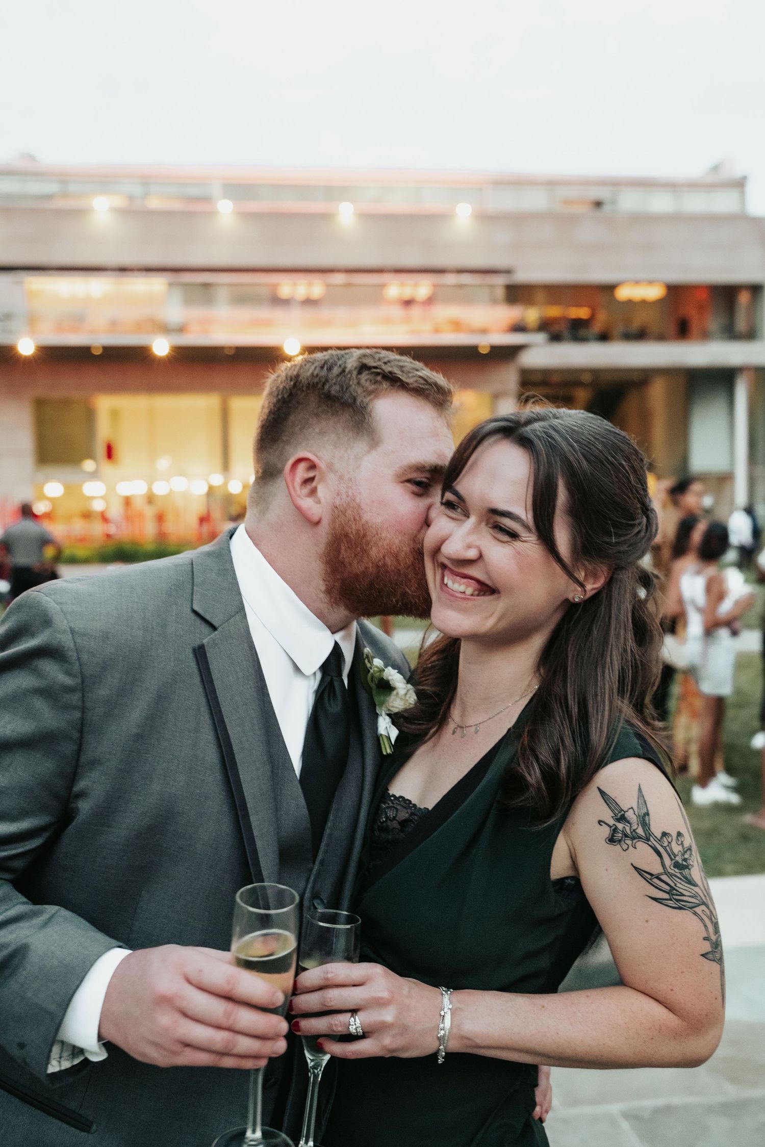Wedding guest leans in to kiss his wife on the cheek in the courtyard of the Virginia Museum of Fine Arts in Richmond Virginia