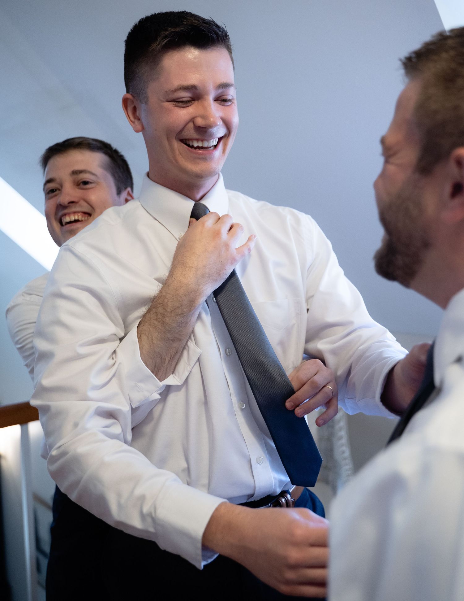 Two groomsmen goof off while fixing the groom's tie as they get ready for his wedding ceremony at Mill at Fine Creek outside Richmond
