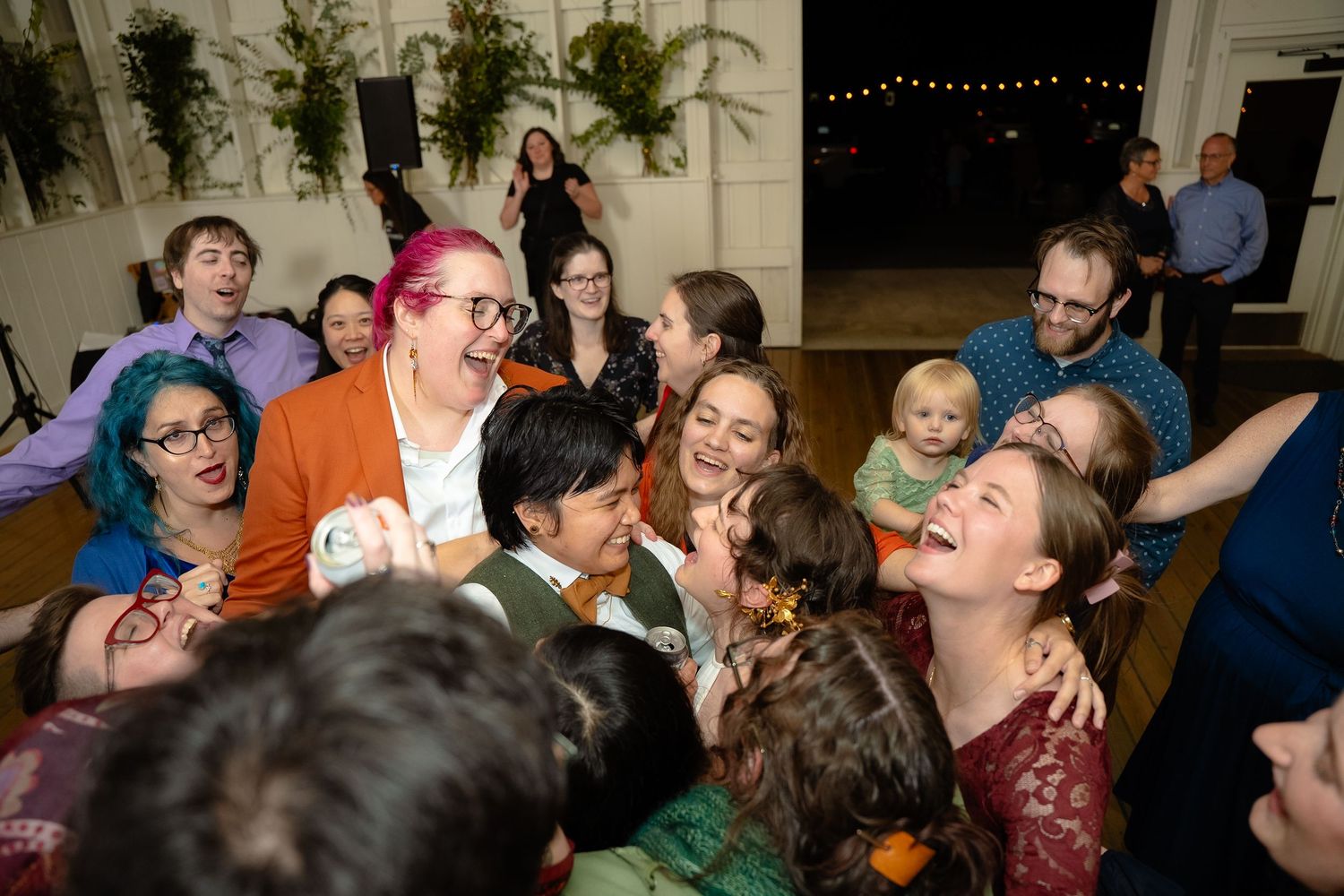 Two lgbtq brides are swarmed by their friends on the dancefloor of their wedding at Valley Road Vineyards in Shenandoah Virginia