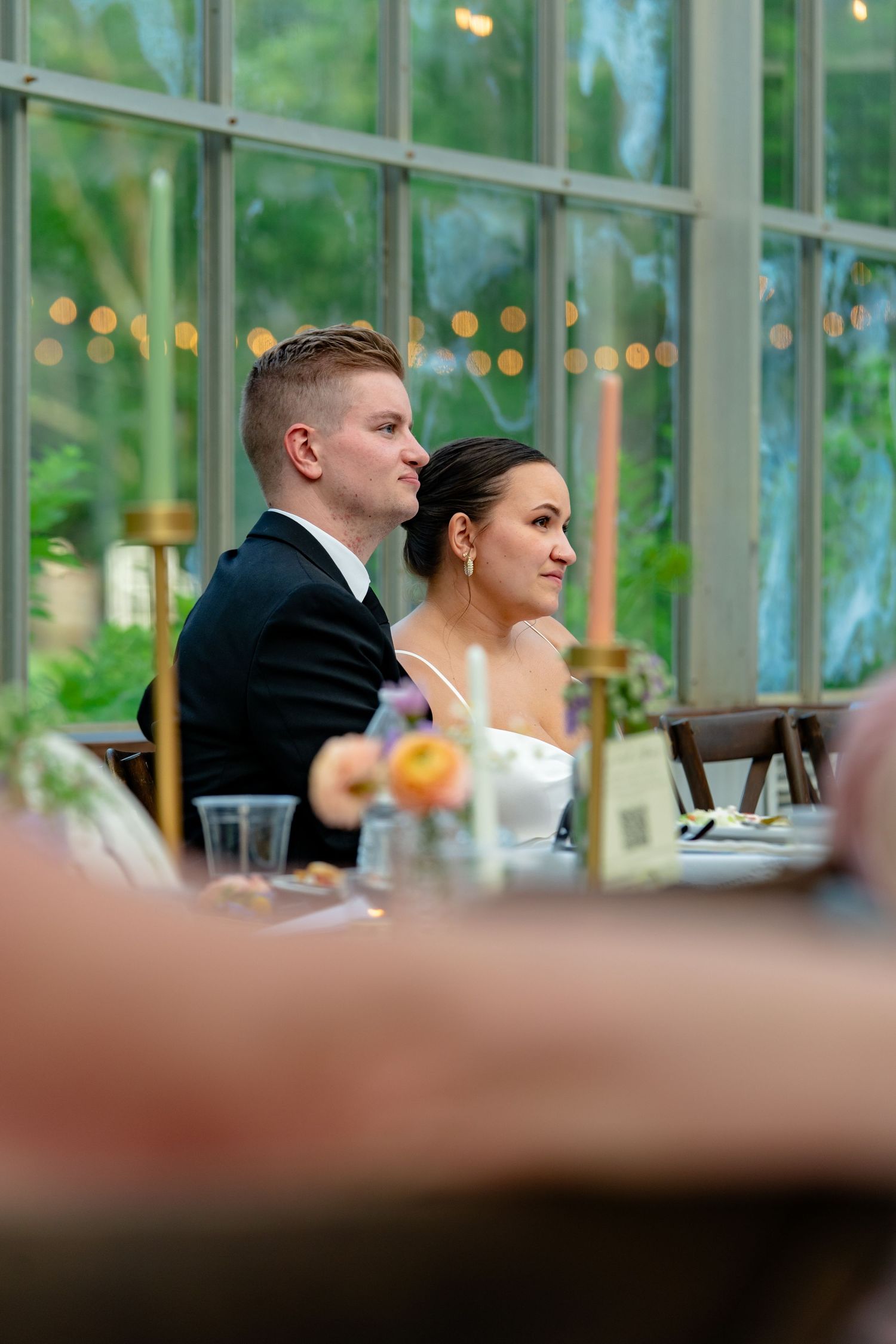 Bride and groom are visibly touched by their guest's heartfelt toasts in the greenhouse dining space of Avonlea Farms