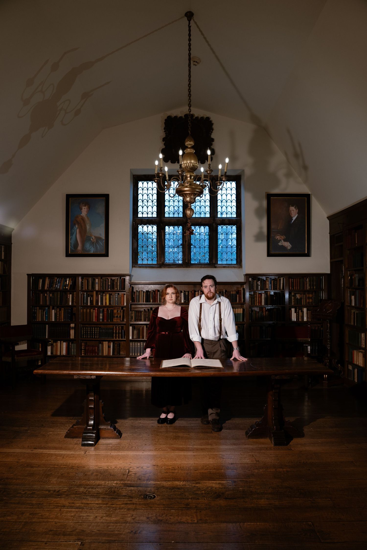 Dark academia photo session in the historic library at the Virginia House museum, engagement shoot features couple in front of table