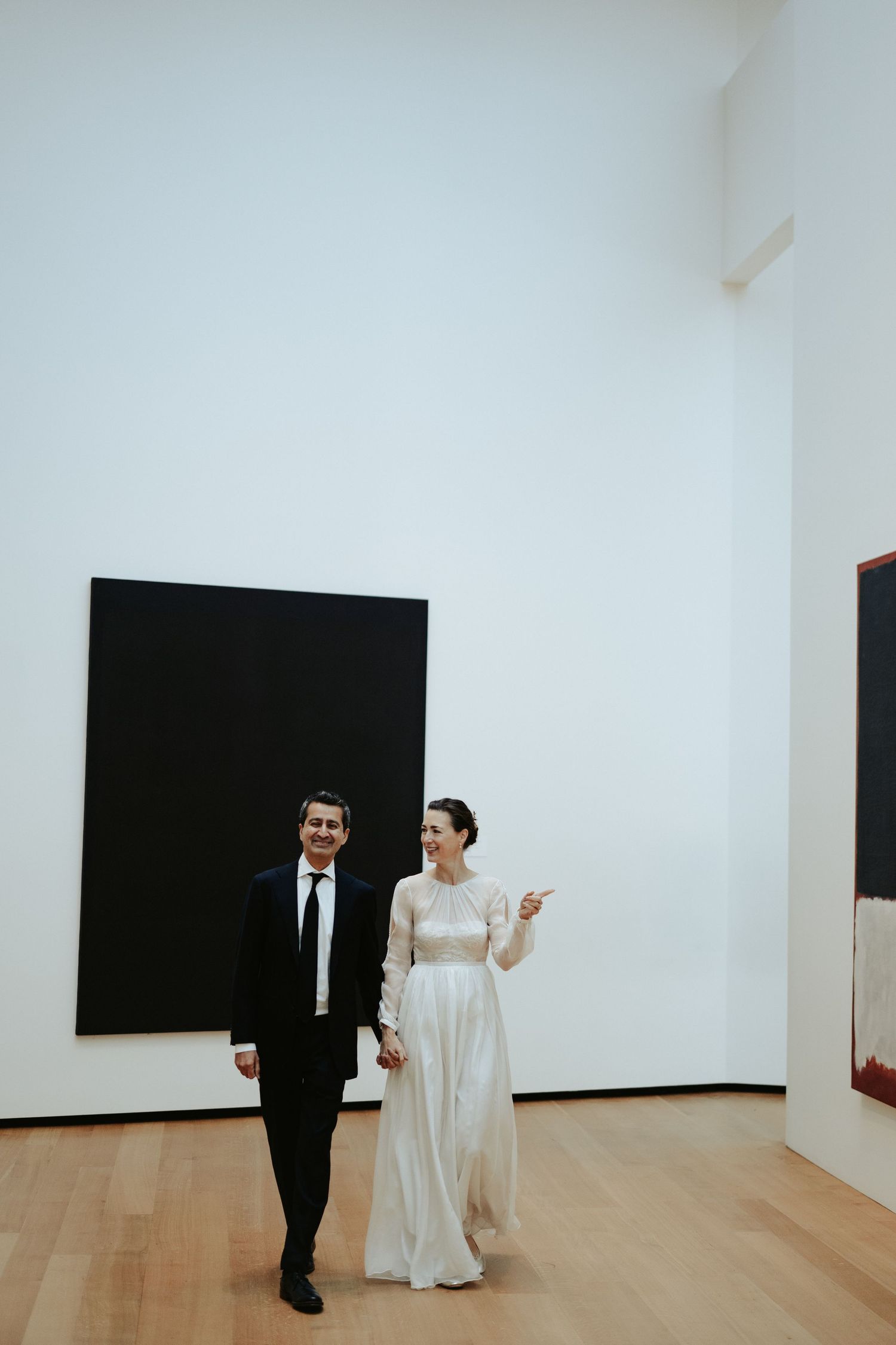 Bride and groom walk through an modern art exhibit with black and white attire which match the black and white art color panels behind them