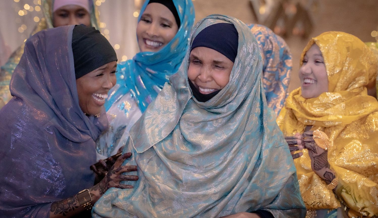Group of women in colorful hijabs laughing and embracing at a festive cultural celebration.