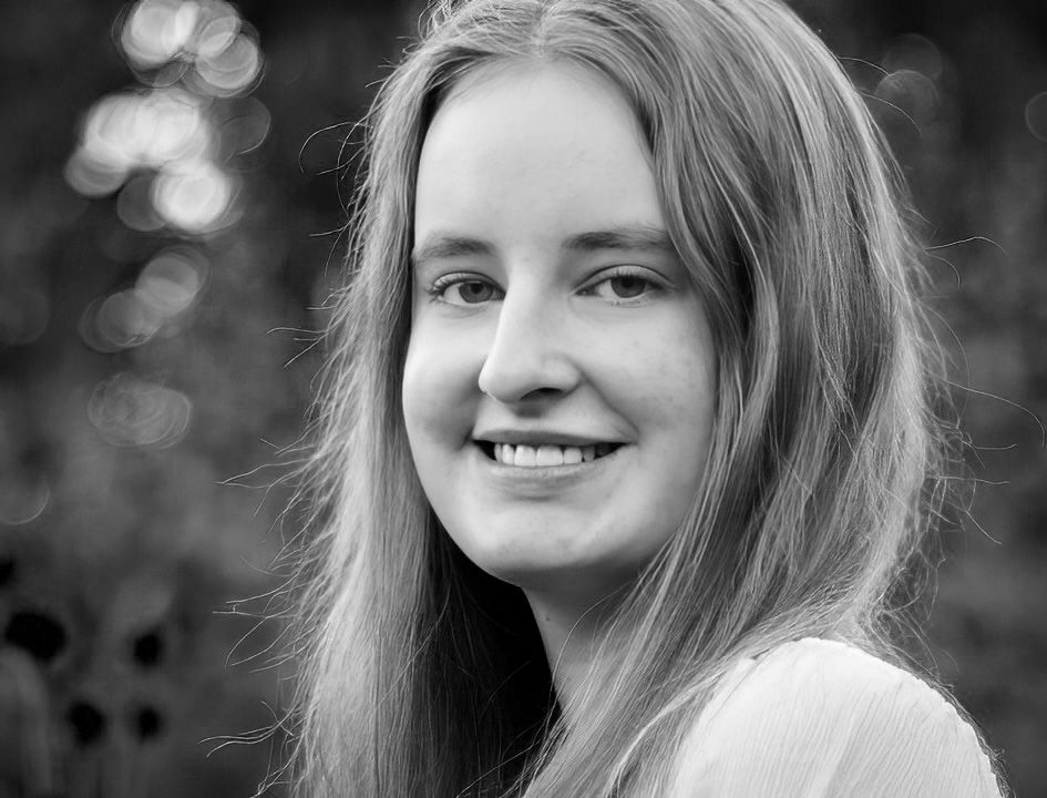 Black and white close-up portrait of a smiling young woman outdoors.