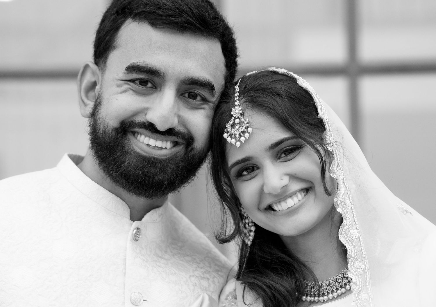 Black and white portrait of South Asian bride and groom smiling together on wedding day.