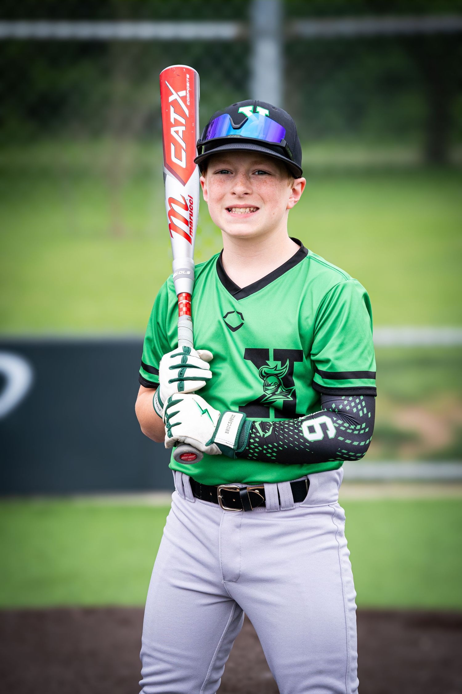 Smiling youth baseball player in green jersey holds red CAT X bat during team photo session.