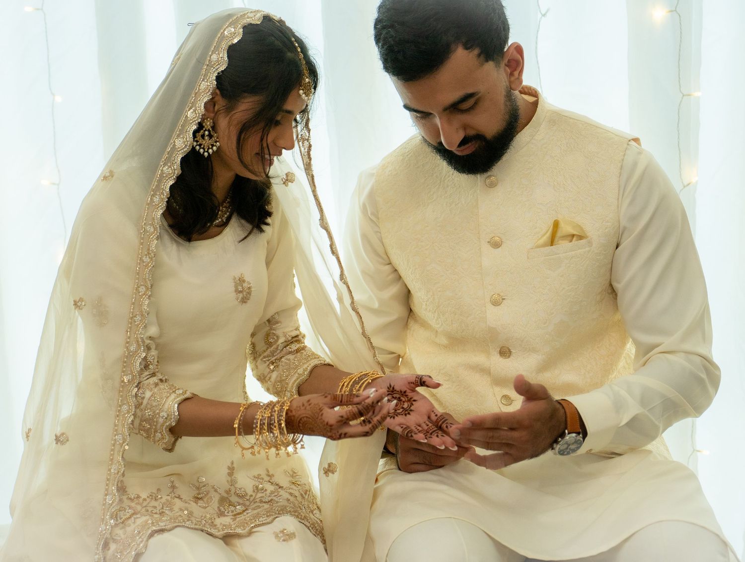 South Asian bride and groom in white outfits exchanging rings at wedding.