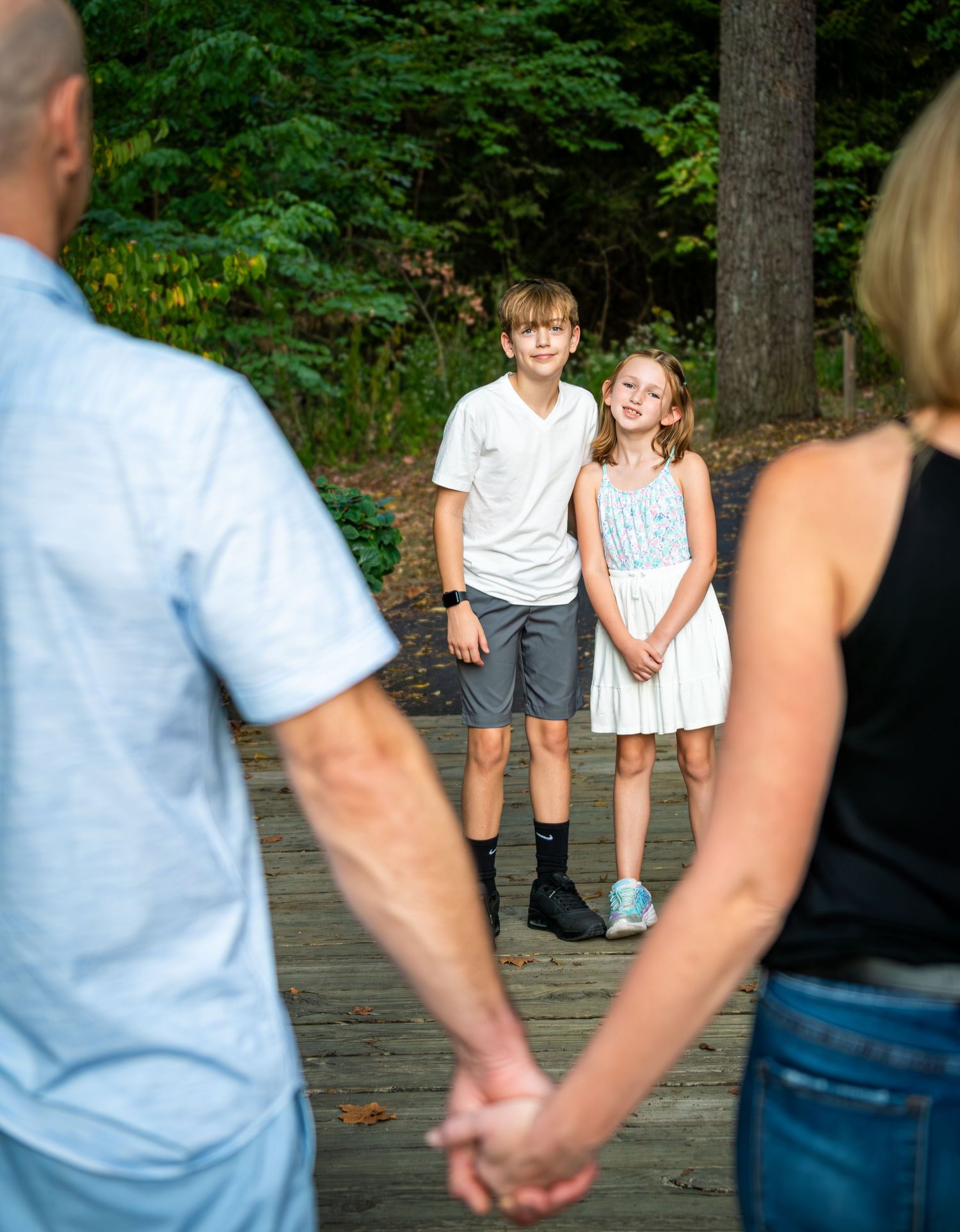 Two children smiling on a wooden bridge while parents hold hands in foreground.