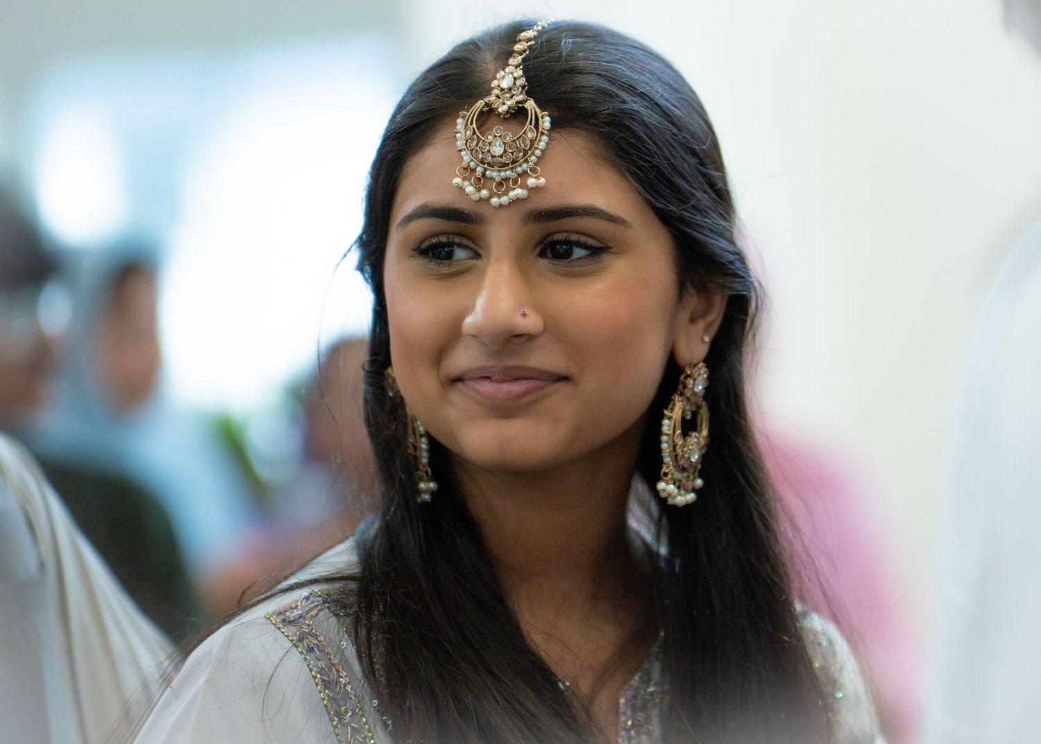 Beautiful South Asian woman smiles softly wearing elegant gold maang tikka and chandelier earrings.