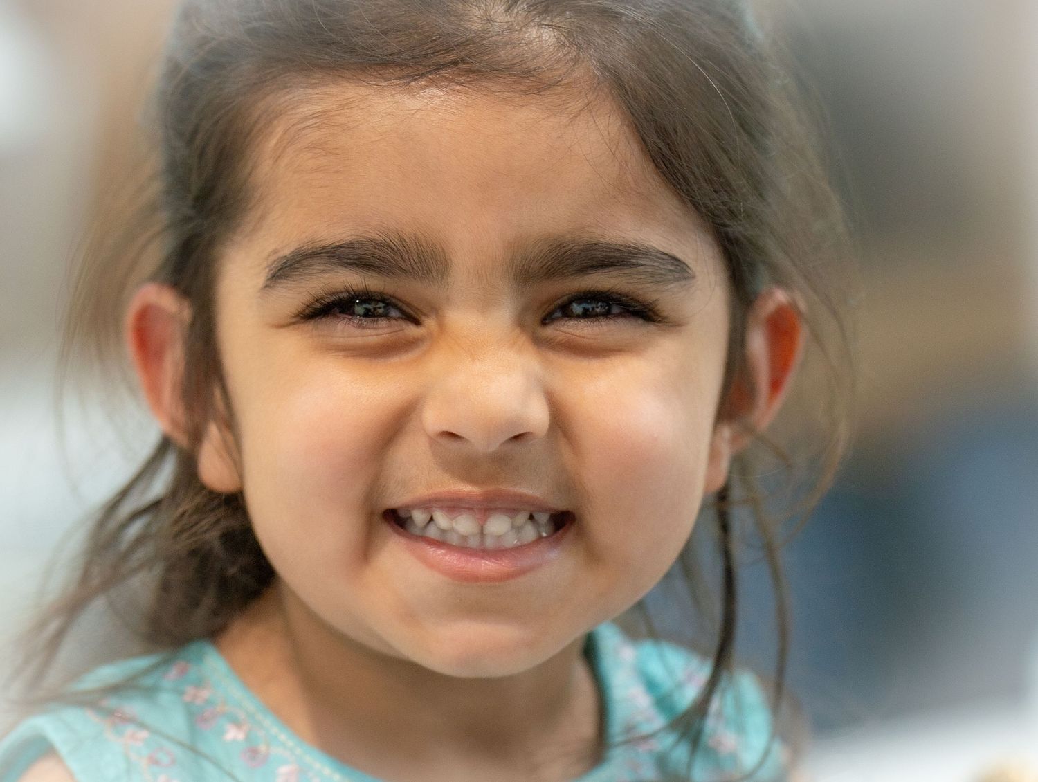 Adorable young South Asian girl with dark hair makes a cute scrunched face smile at the camera.