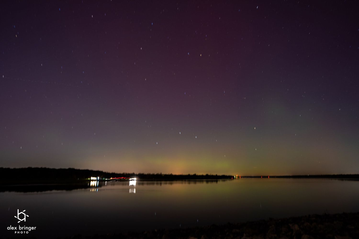 Northern lights aurora borealis reflecting purple and green hues over a calm lake at night.