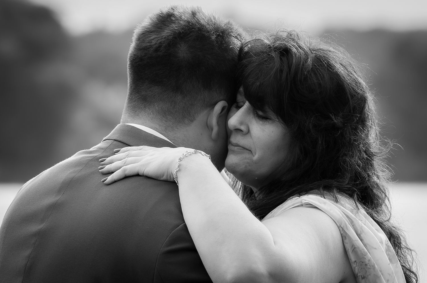 Black and white photo of a couple embracing tenderly at a wedding, woman resting her head on mans shoulder.