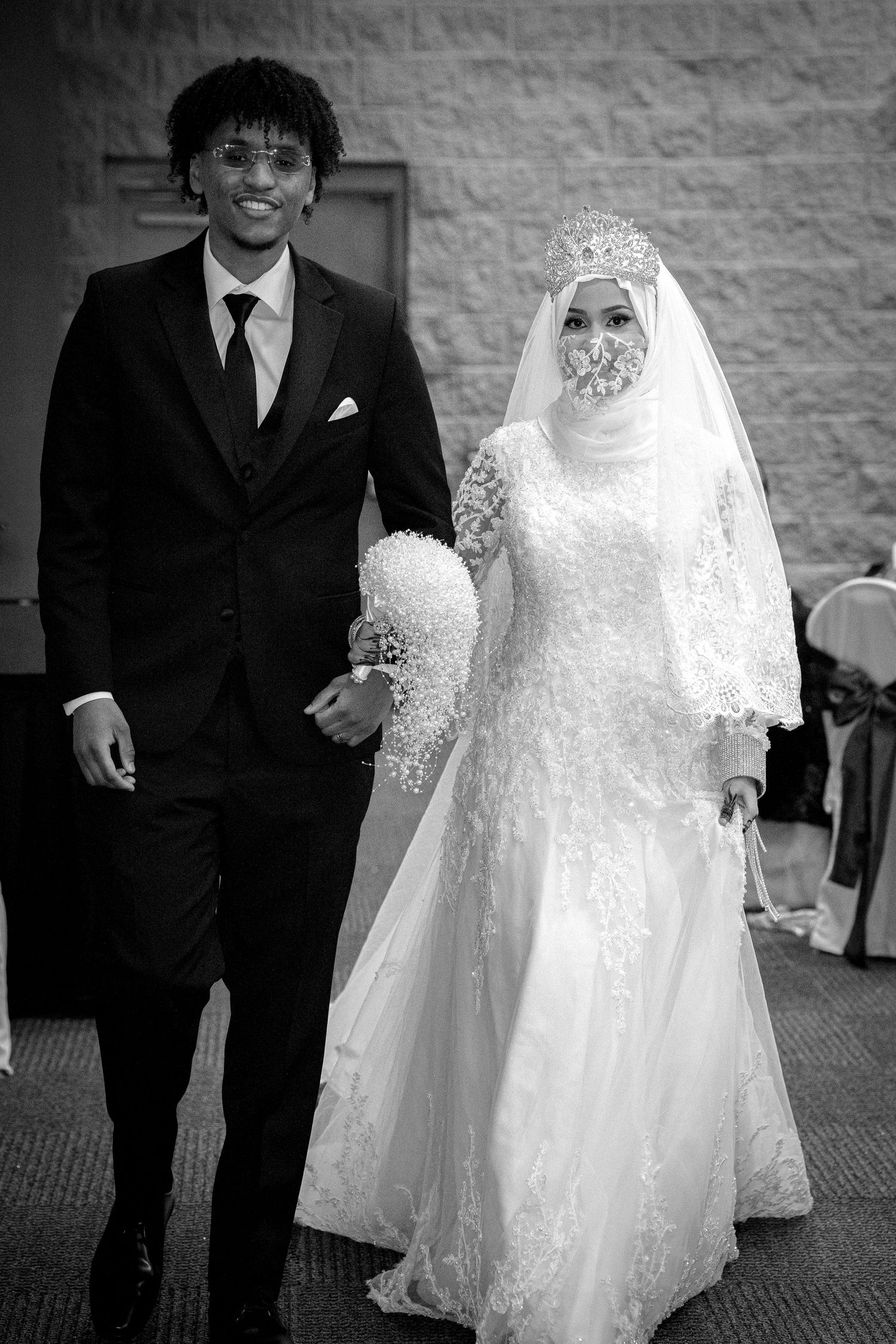 Black and white portrait of a Muslim bride and groom walking together at their wedding ceremony.