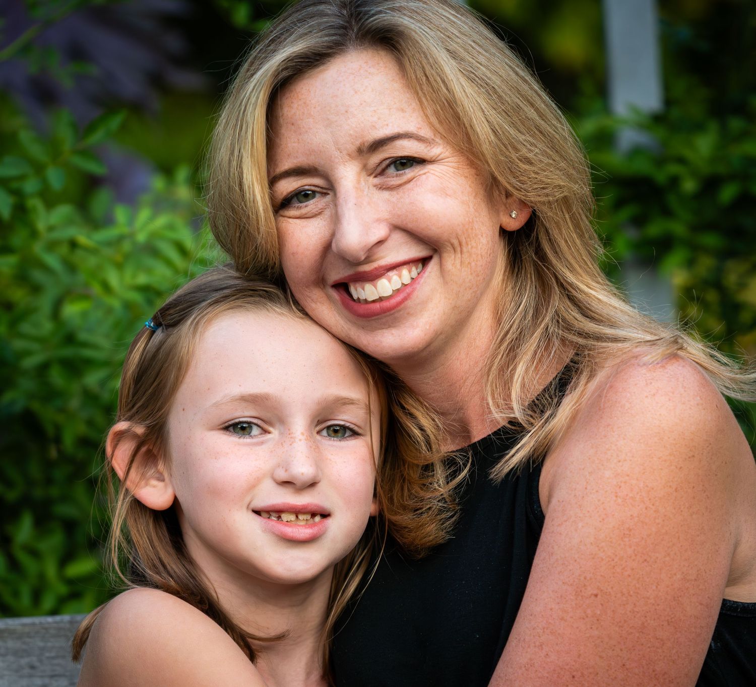 Smiling mother and young daughter posing cheek to cheek in outdoor portrait.