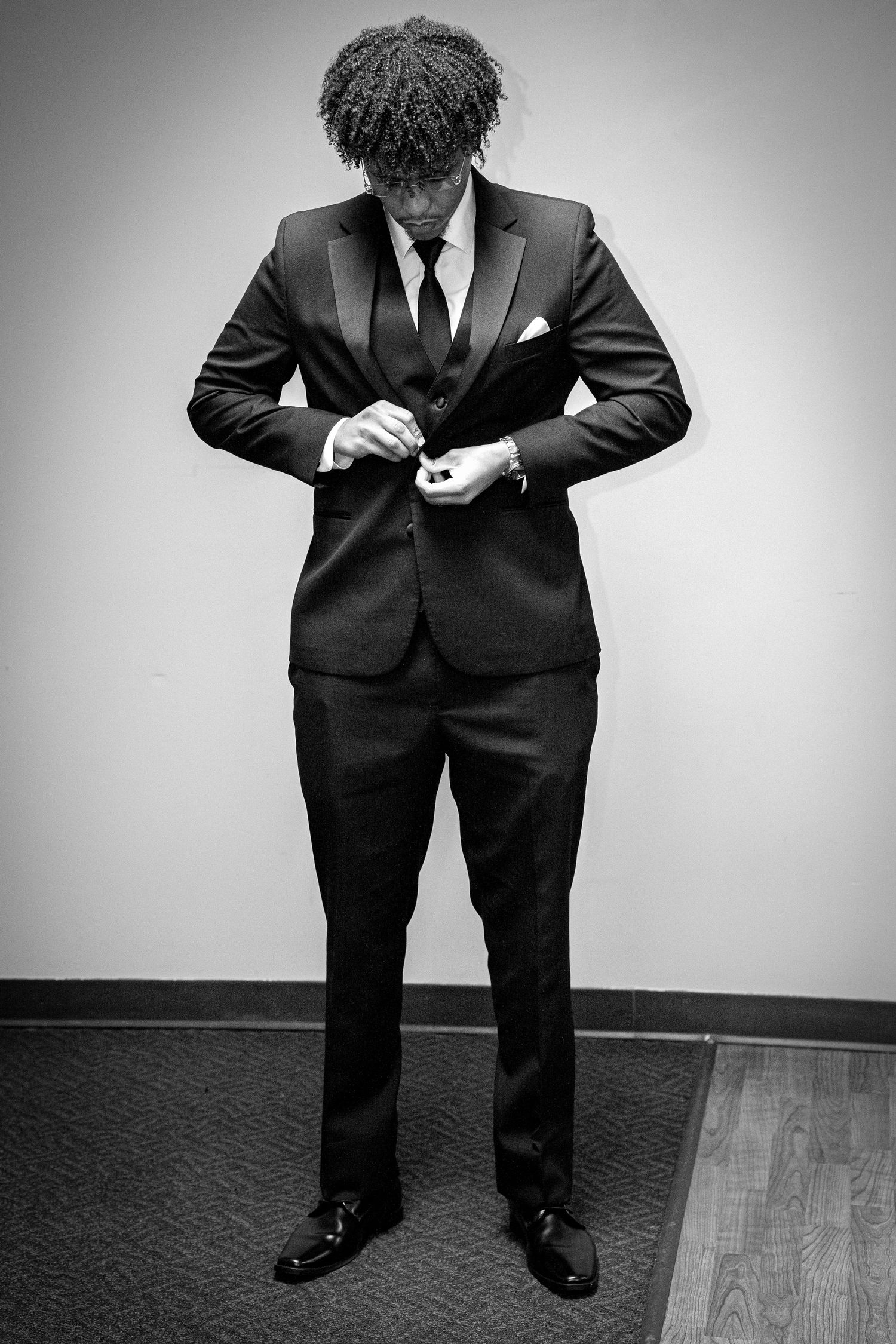 Elegant man in black suit adjusting cufflinks in black and white formal portrait photo.