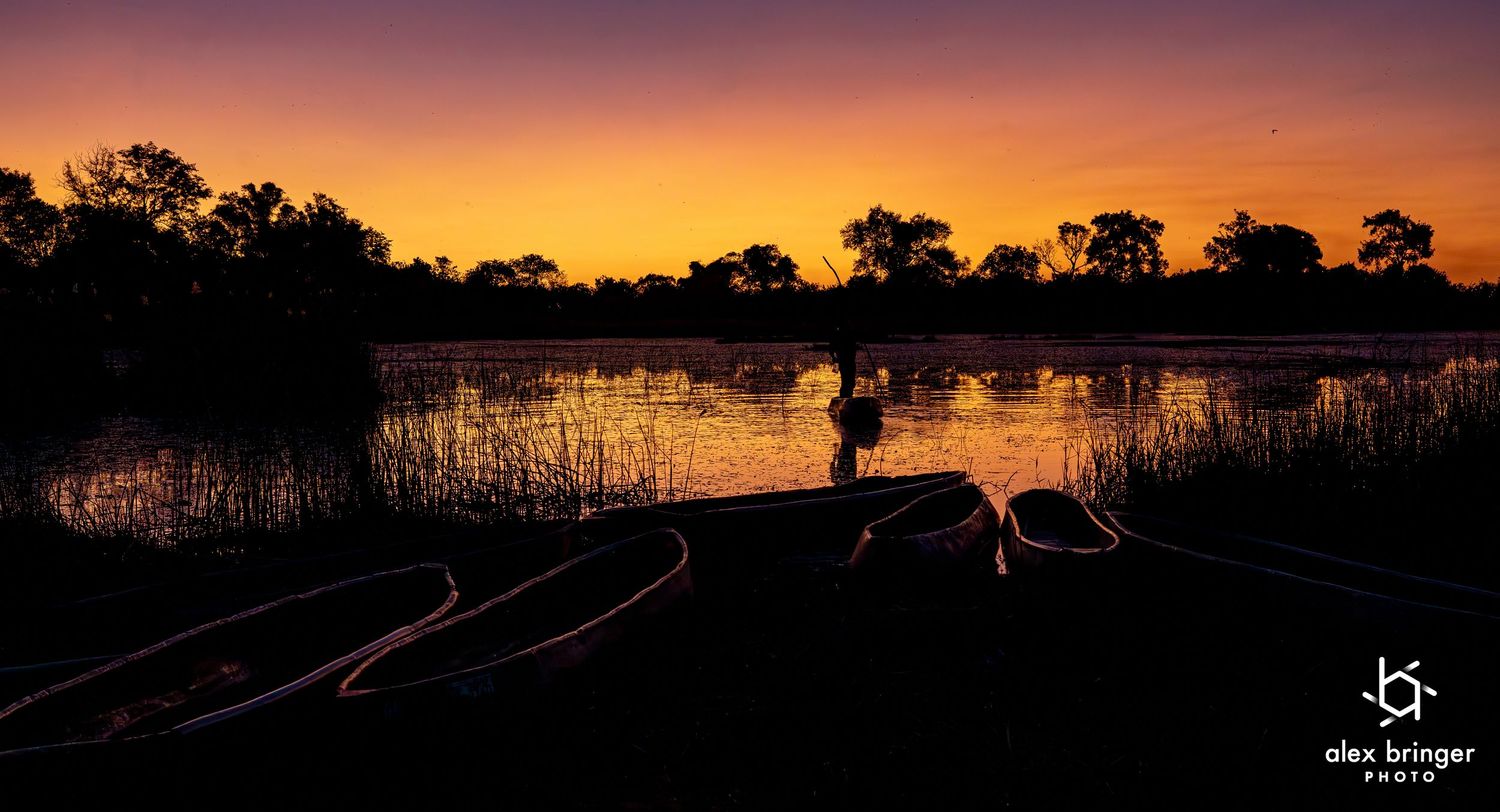 Silhouette of a person on a boat at sunset over a calm river with vibrant orange and purple sky reflections.