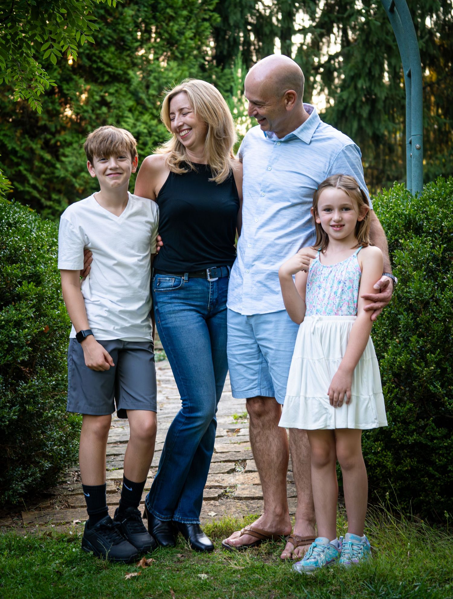 Happy family of four posing together in a lush garden setting, smiling warmly for a portrait photo.