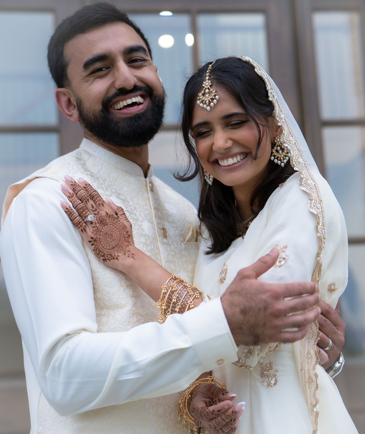Joyful South Asian wedding couple embracing, bride displaying beautiful mehndi and gold jewelry.