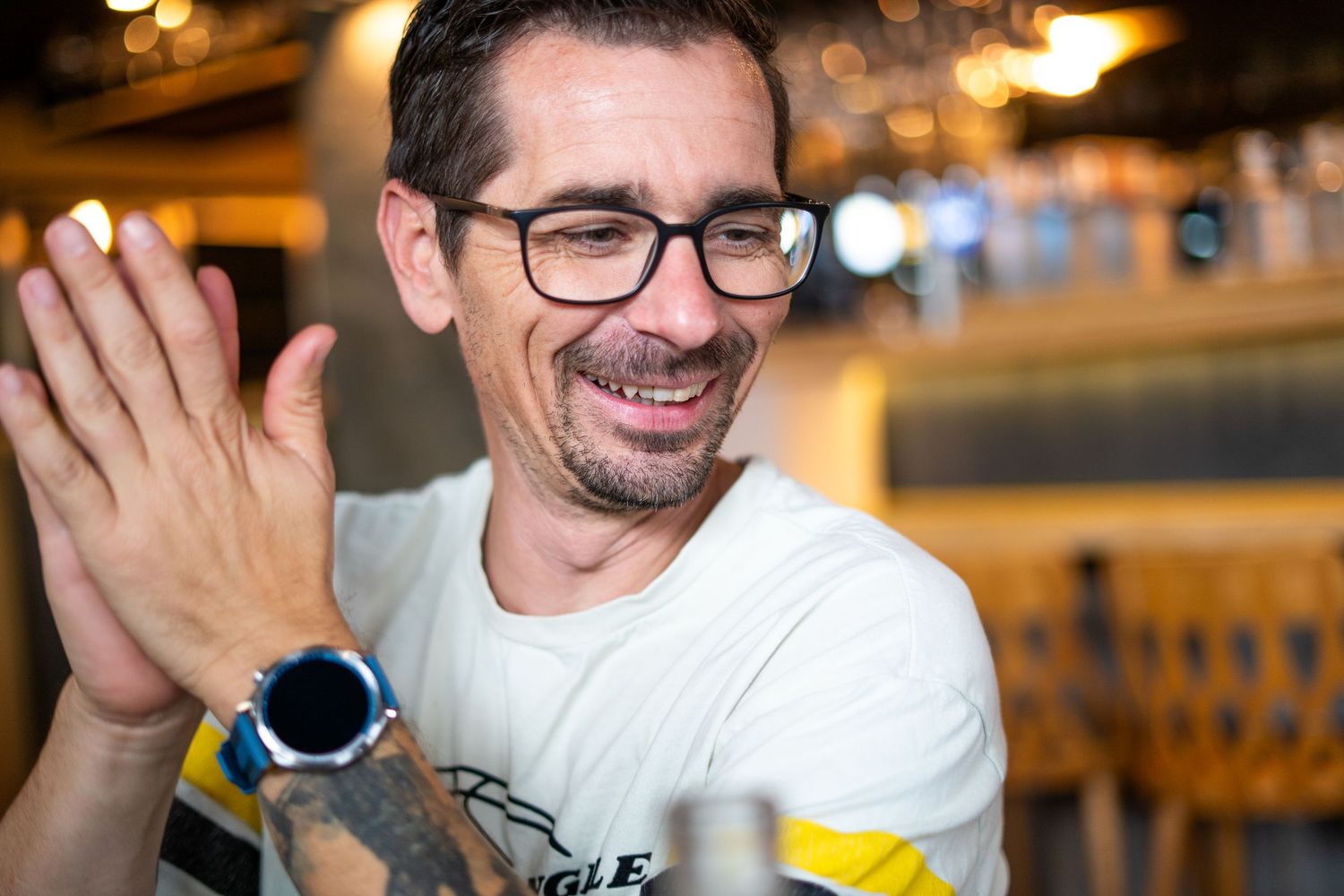 Smiling man with glasses examining a bottle in a bar setting.