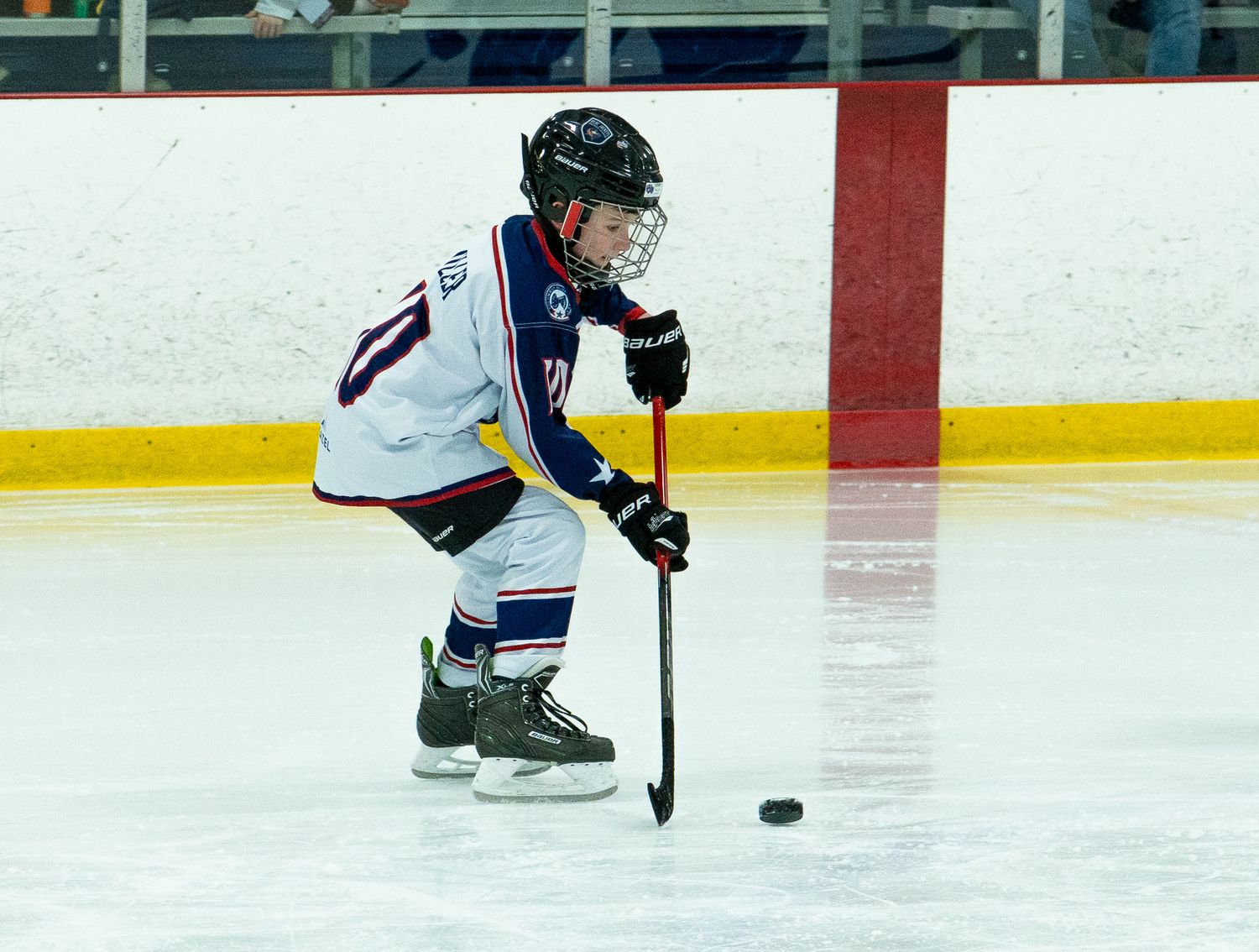 Young hockey player in navy uniform controlling puck during indoor ice rink game.