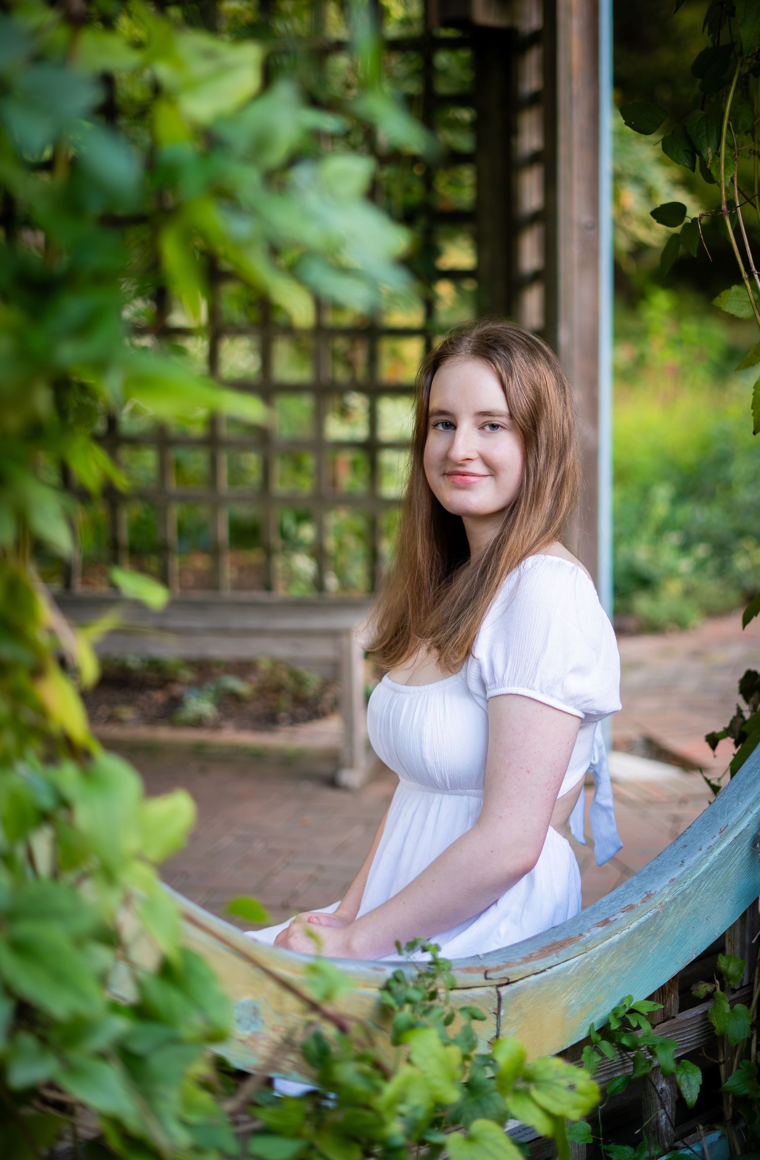 Young woman in white dress sitting on bench in lush garden setting.