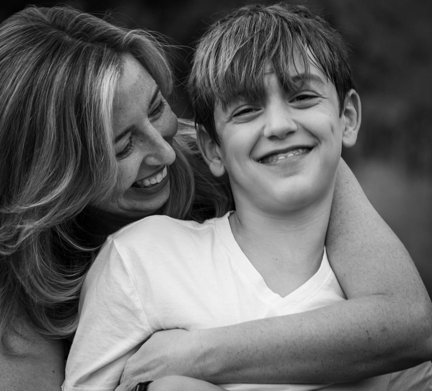 Mother hugging her smiling son in a warm black and white candid portrait.