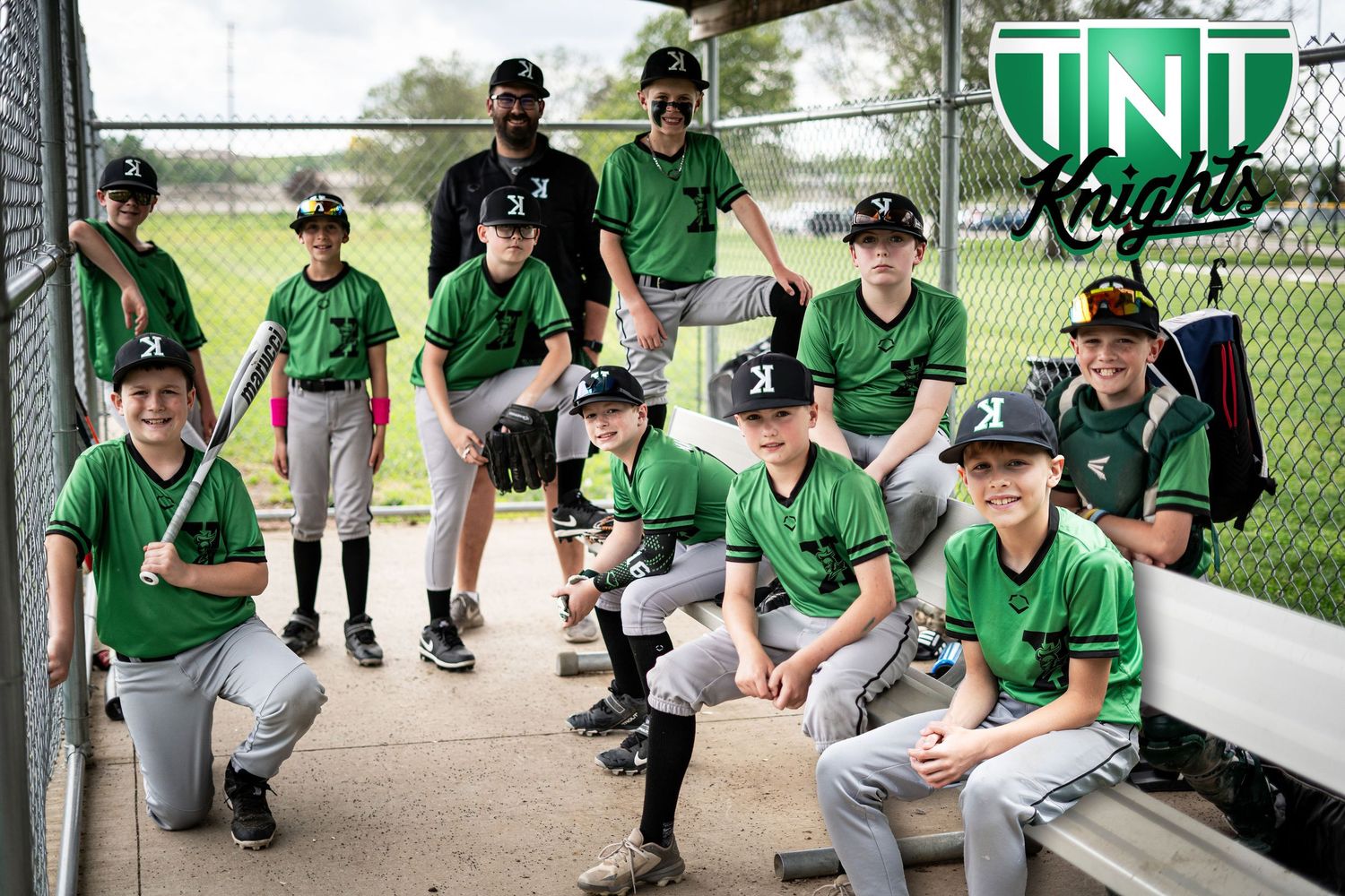 TNT Knights youth baseball team poses together in green uniforms in dugout for team photo.